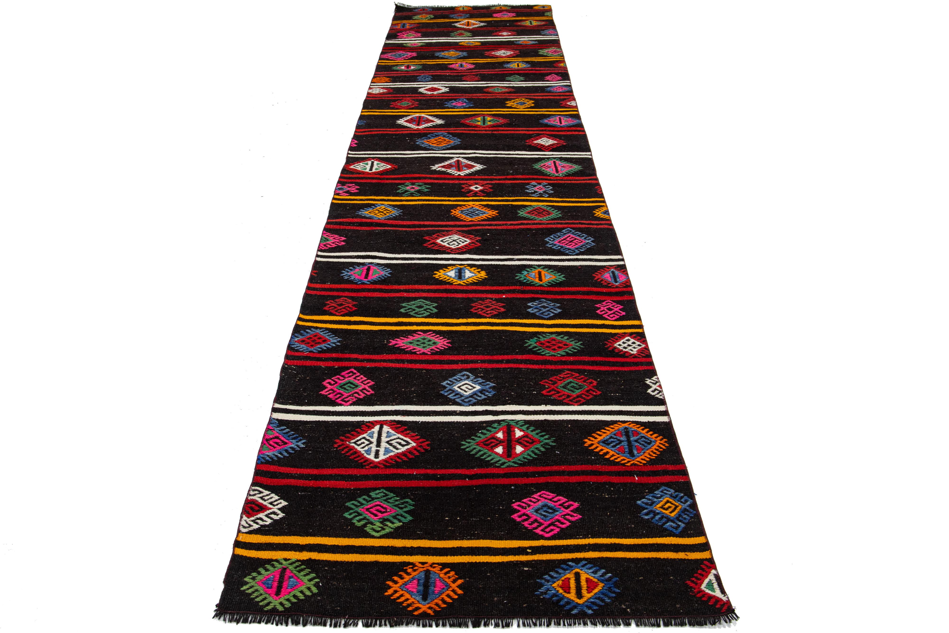 Lebendiger Kelimteppich aus Wolle mit geometrischem Muster auf schwarzem Hintergrund.

Dieser Teppich misst 3' x 12'10