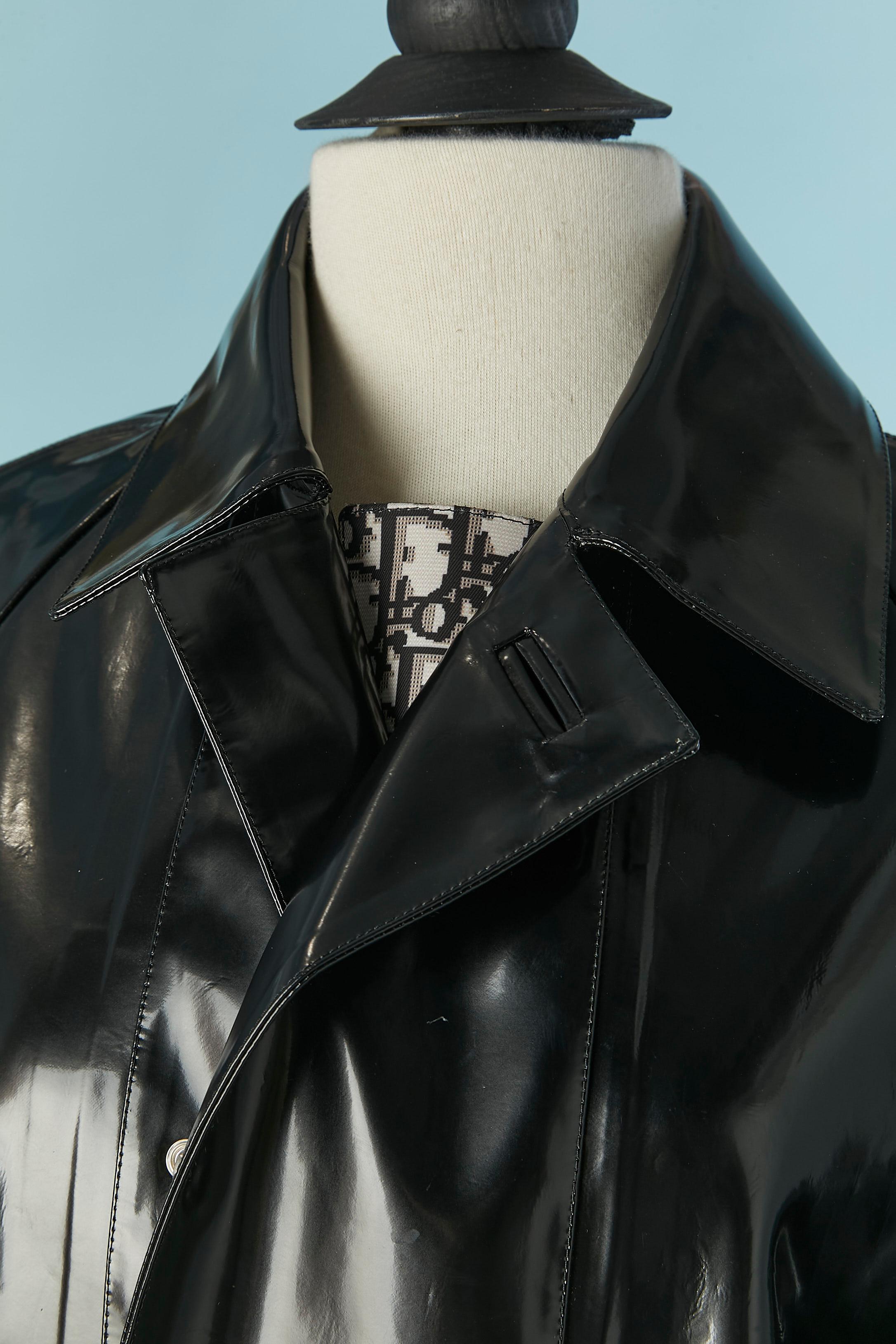 Manteau en vinyle noir (ou en canevas enduit) avec patte de boutonnage en canevas de marque. Double fermeture à pression sur le milieu du devant. Fendu au milieu du dos (longueur = 57cm) avec fermeture à bouton-pression. Manches raglan. Pochette sur