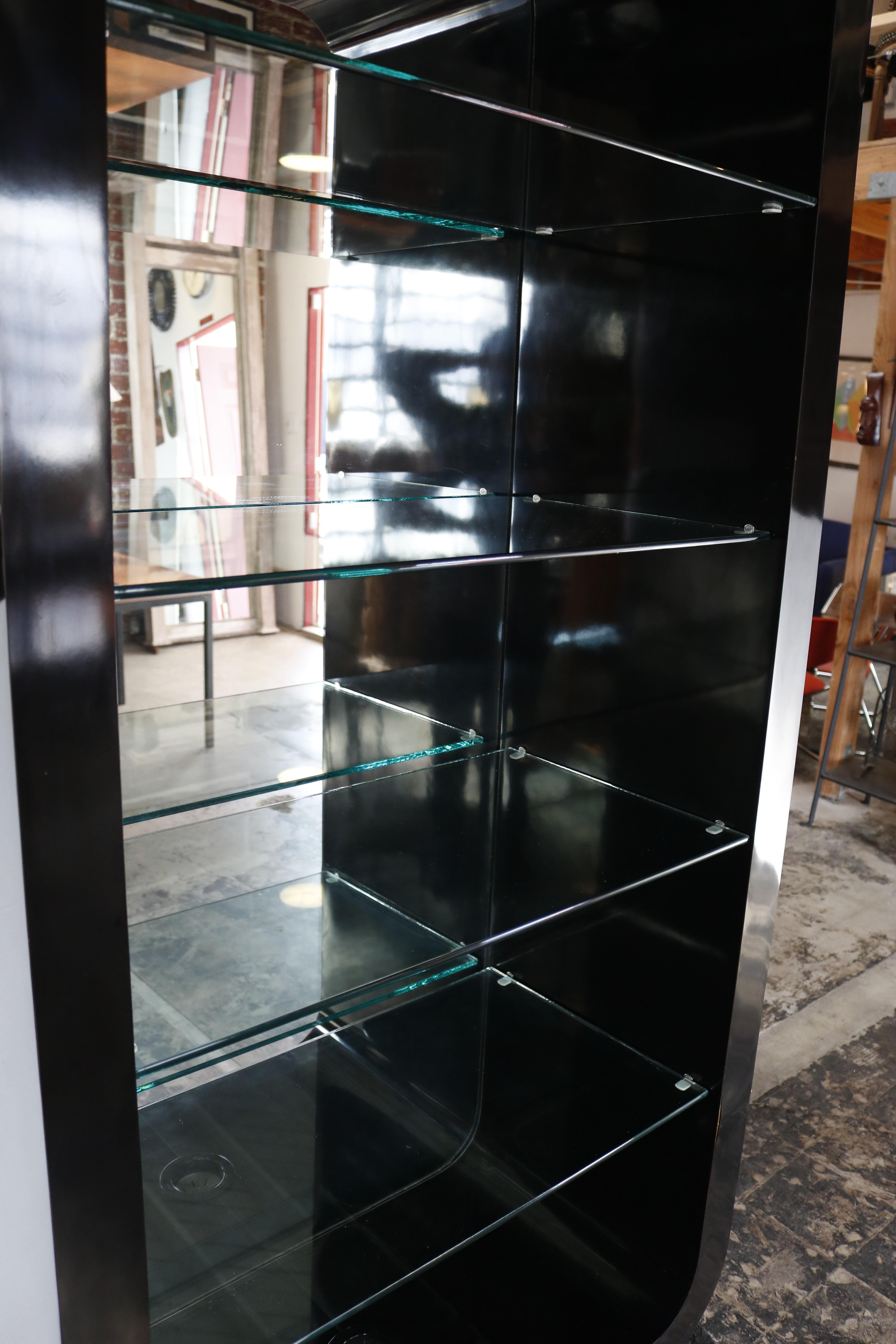 A sheen black vitrine with glass shelving and recess lighting on the inside top and bottom of the piece.
It is made of Formica and looks exactly like lacquer which makes it much less fragile.