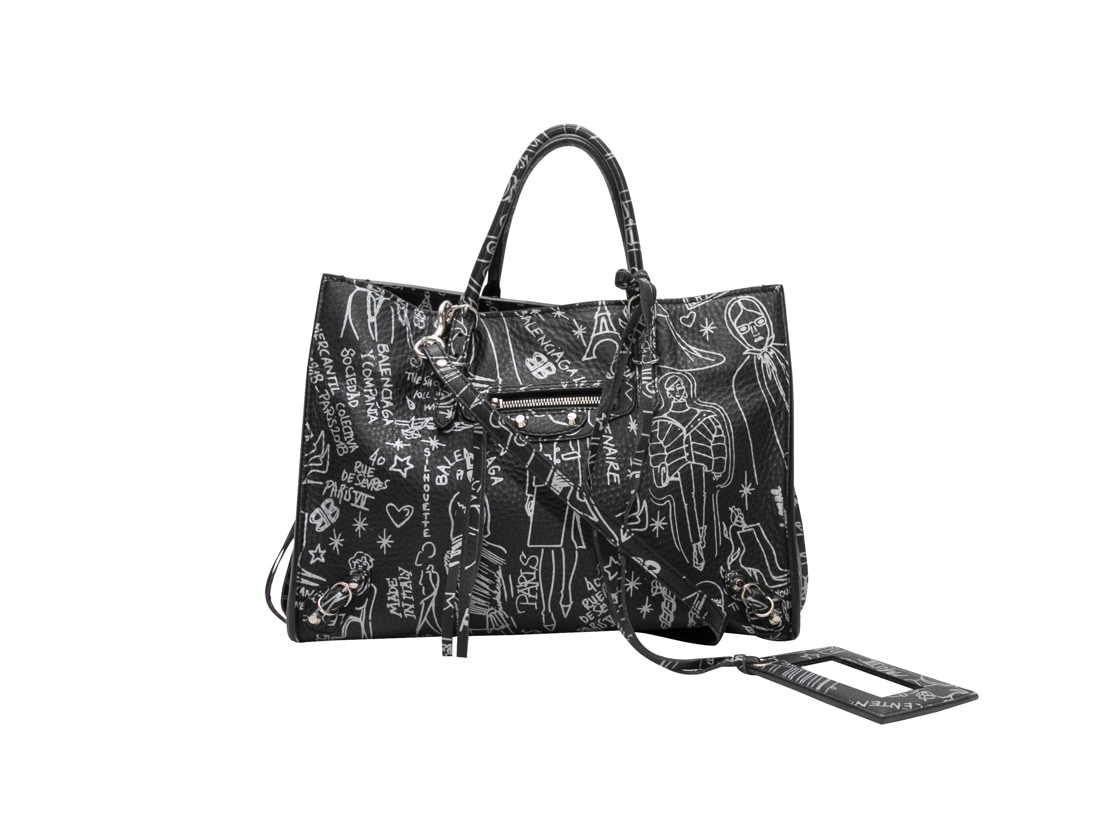Product Details: Black & White Balenciaga Small Graffiti Tote. This tote features a leather body, silver-tone hardware, dual flat top handles, an exterior zip pocket, and an optional shoulder strap. 10