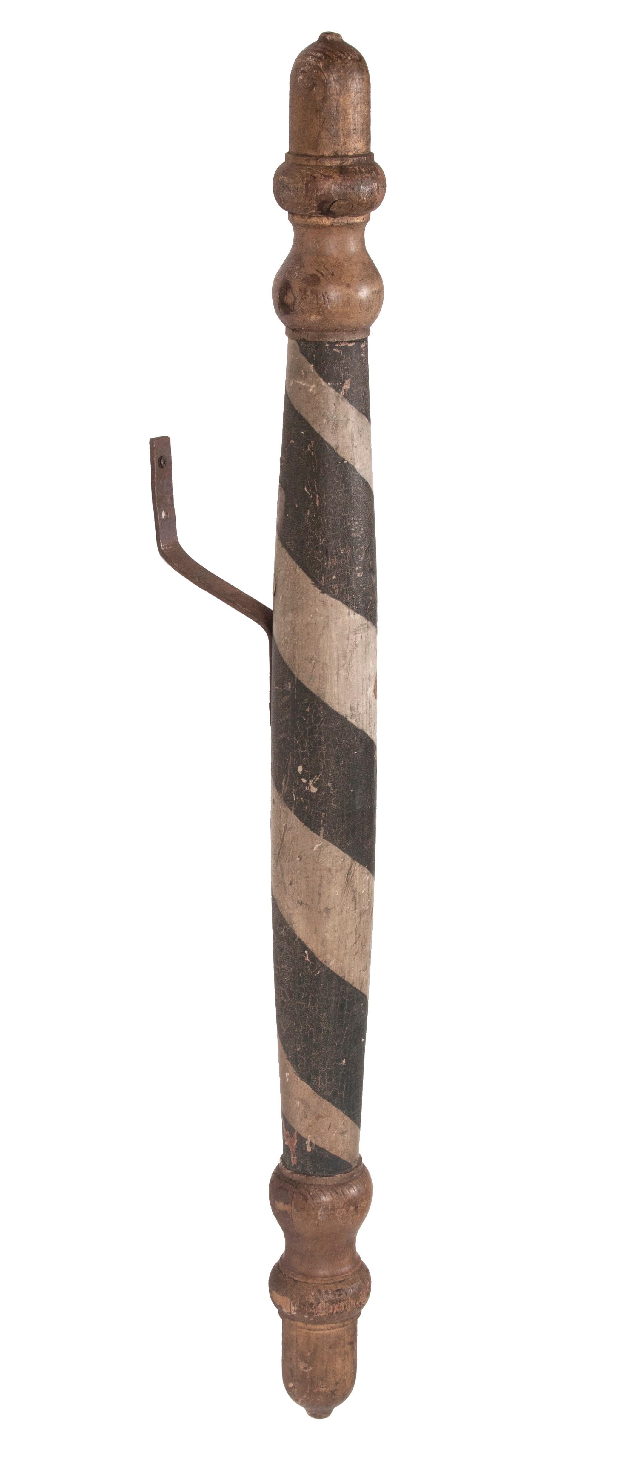 This delicate, New England barber pole has a round, double-tapered shaft with a swelled vase turning above and below, capped at each end with a elongated acorn finial. The center of the pole is painted black and white in the typical, swirling helix,