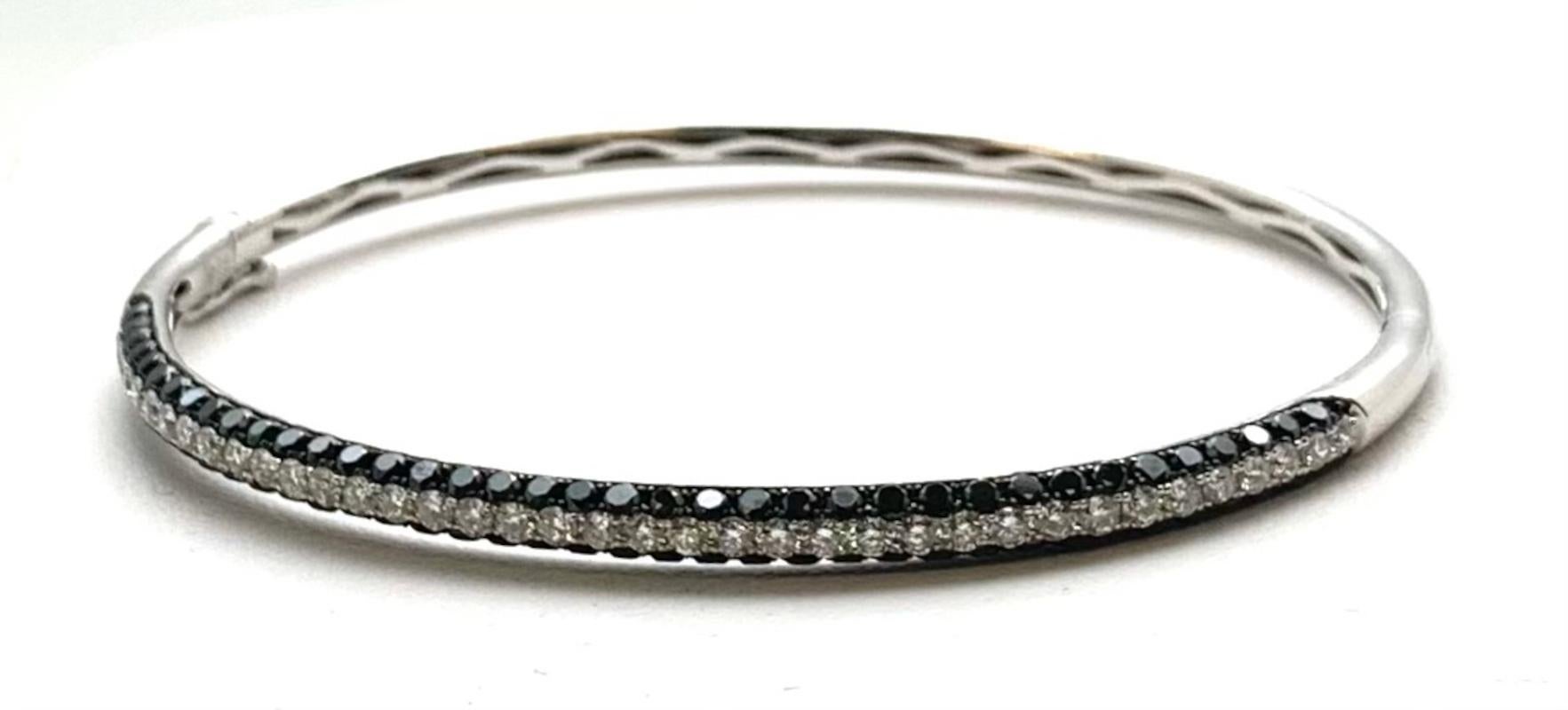 This beautiful hinged bangle bracelet features 3.56 carats of black and white diamonds pave set in 18k white gold. A center row of brilliant white diamonds is outlined on either side by a row of gorgeous and dramatic black diamonds. The bangle