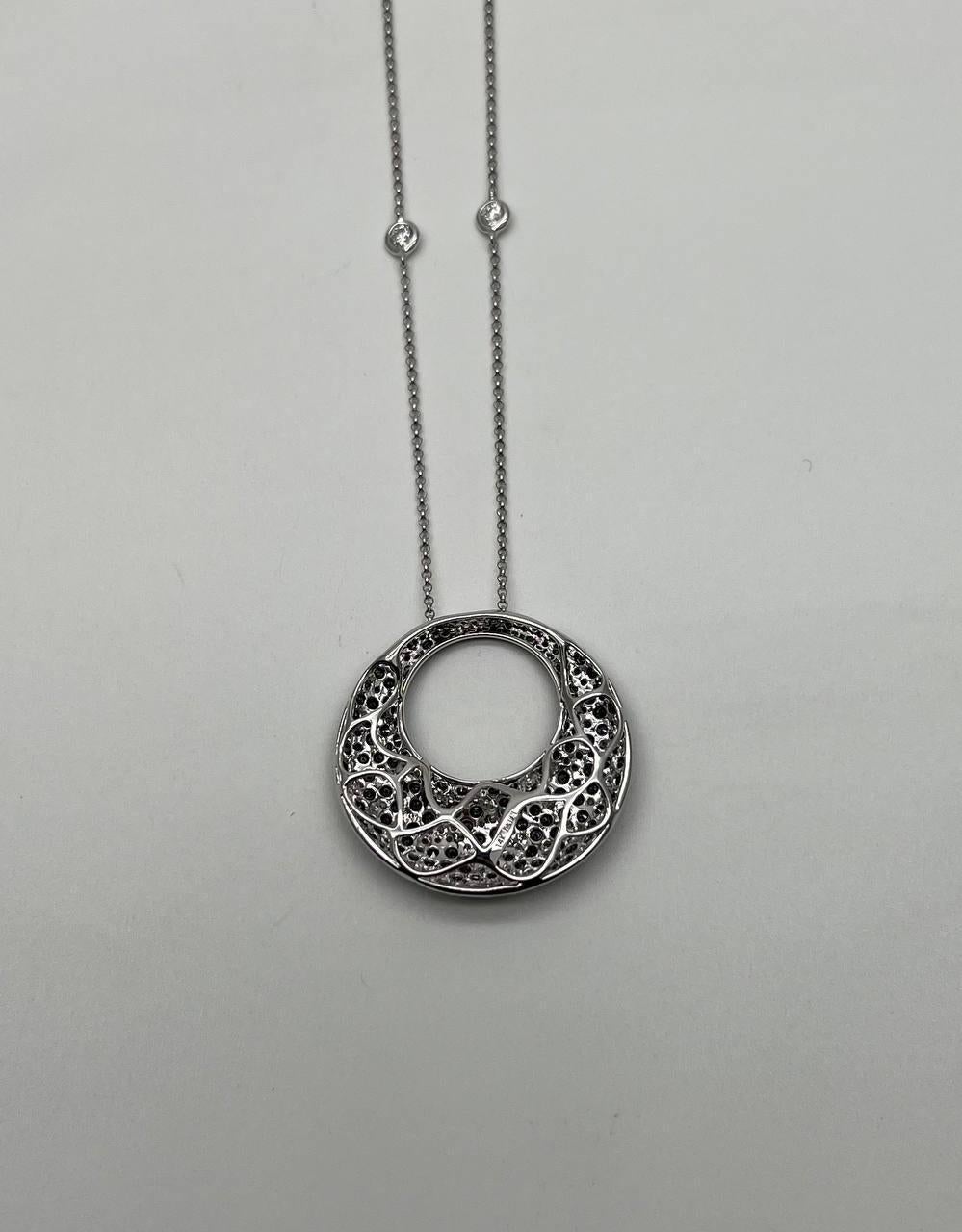 A captivating pendant necklace featuring a circular design with a speckled pattern of pave-set black & white diamonds. The piece is crafted with precision, showcasing a harmonious blend of textures and finishes. 14K White Gold. 7.50 CTW Natural
