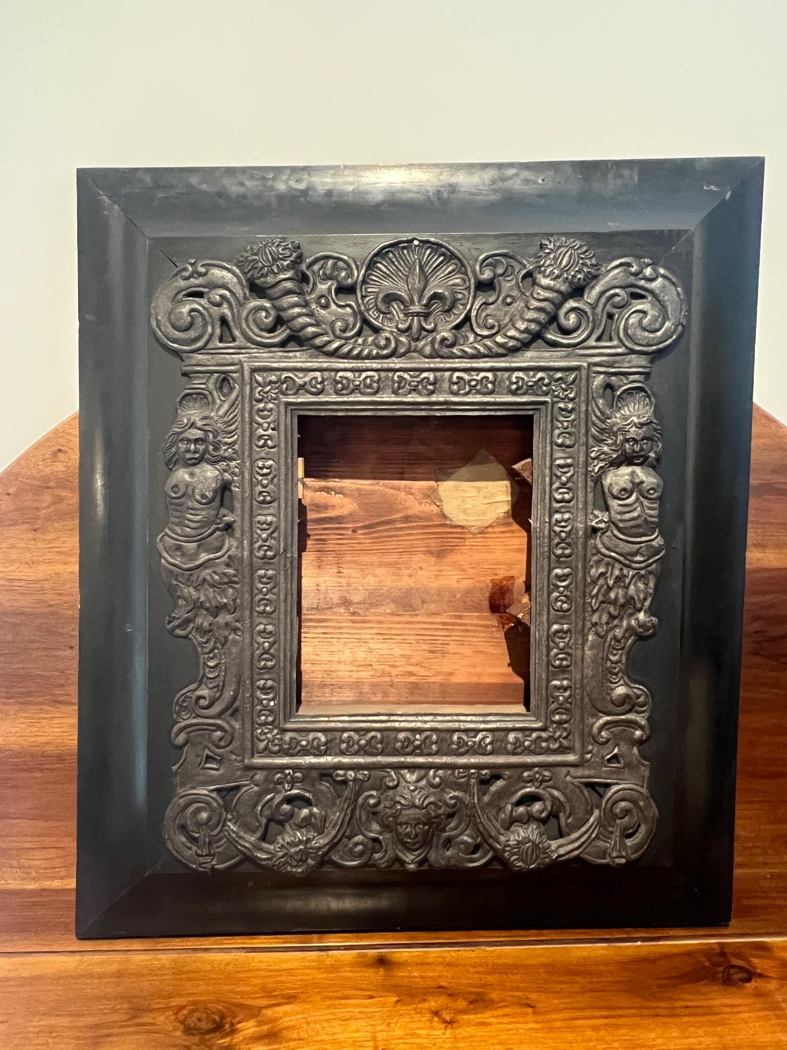 This imposing frame has a large coved wood outer border with an intricately detailed pressed tin or tole overlay. The pressed metal has a lot going on: Fleur de Lis, Cornucopia and topless mermaids. Also, swags, rosettes, flames and shells add to