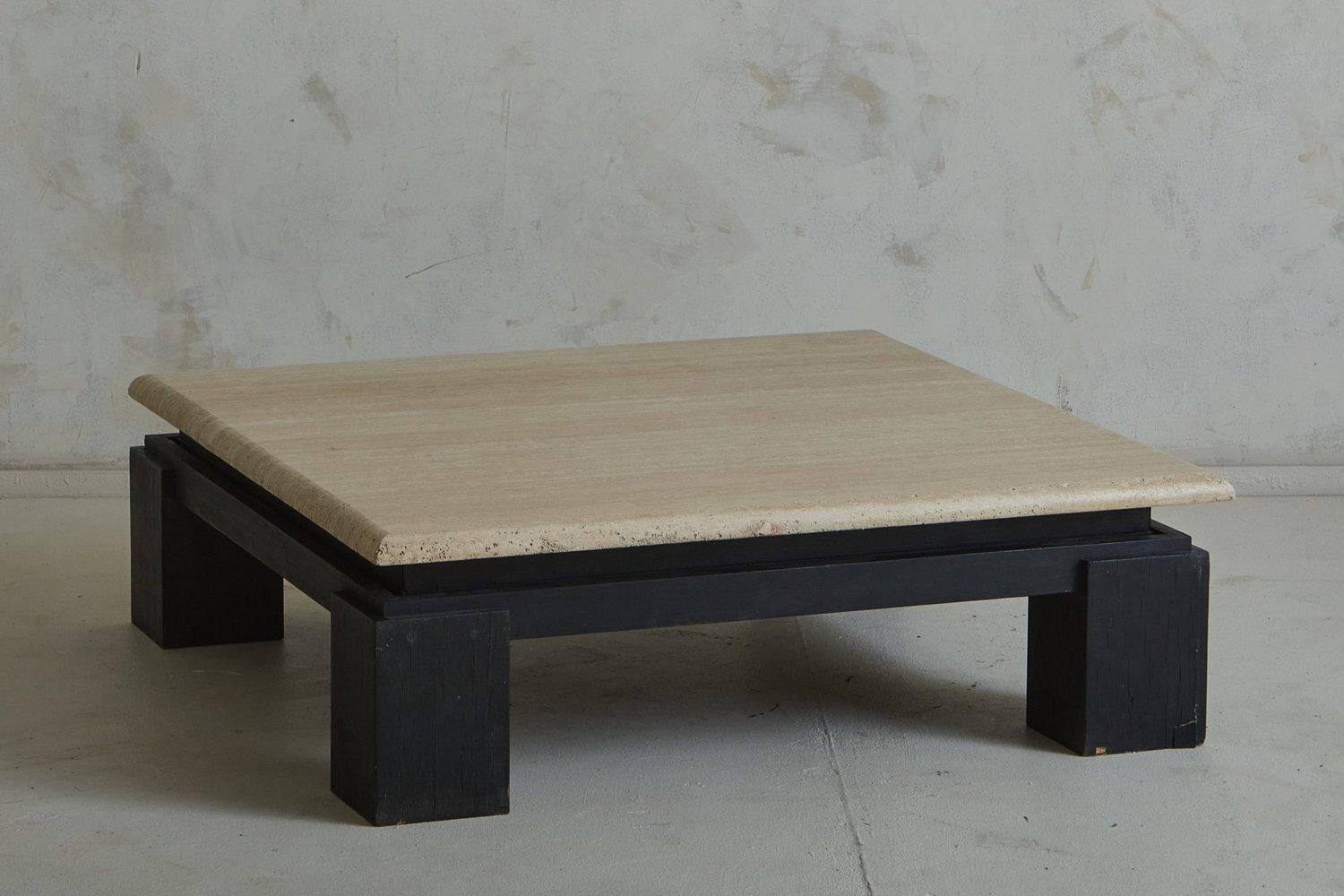 A vintage French coffee table featuring a handsome black painted wood base with block legs. This piece has a square travertine table top with beautiful veining and a beveled edge, which appears to float above the base. Sourced in France, 20th