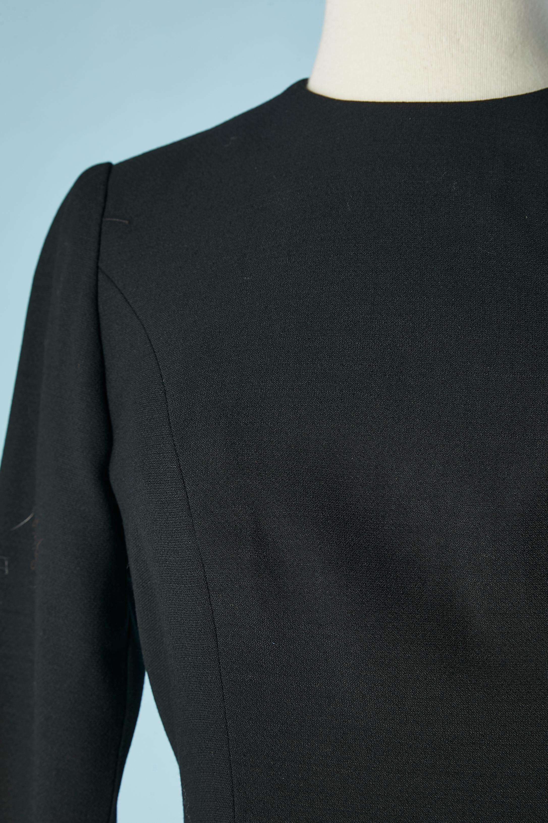 Vestido de cóctel de lana negra con pliegues laterales y pasamanería. No hay etiqueta de composición del tejido, pero probablemente el forro sea de acetato. 
Cierre de cremallera invisible en la parte central de la espalda y en los puños. 
TALLA 38