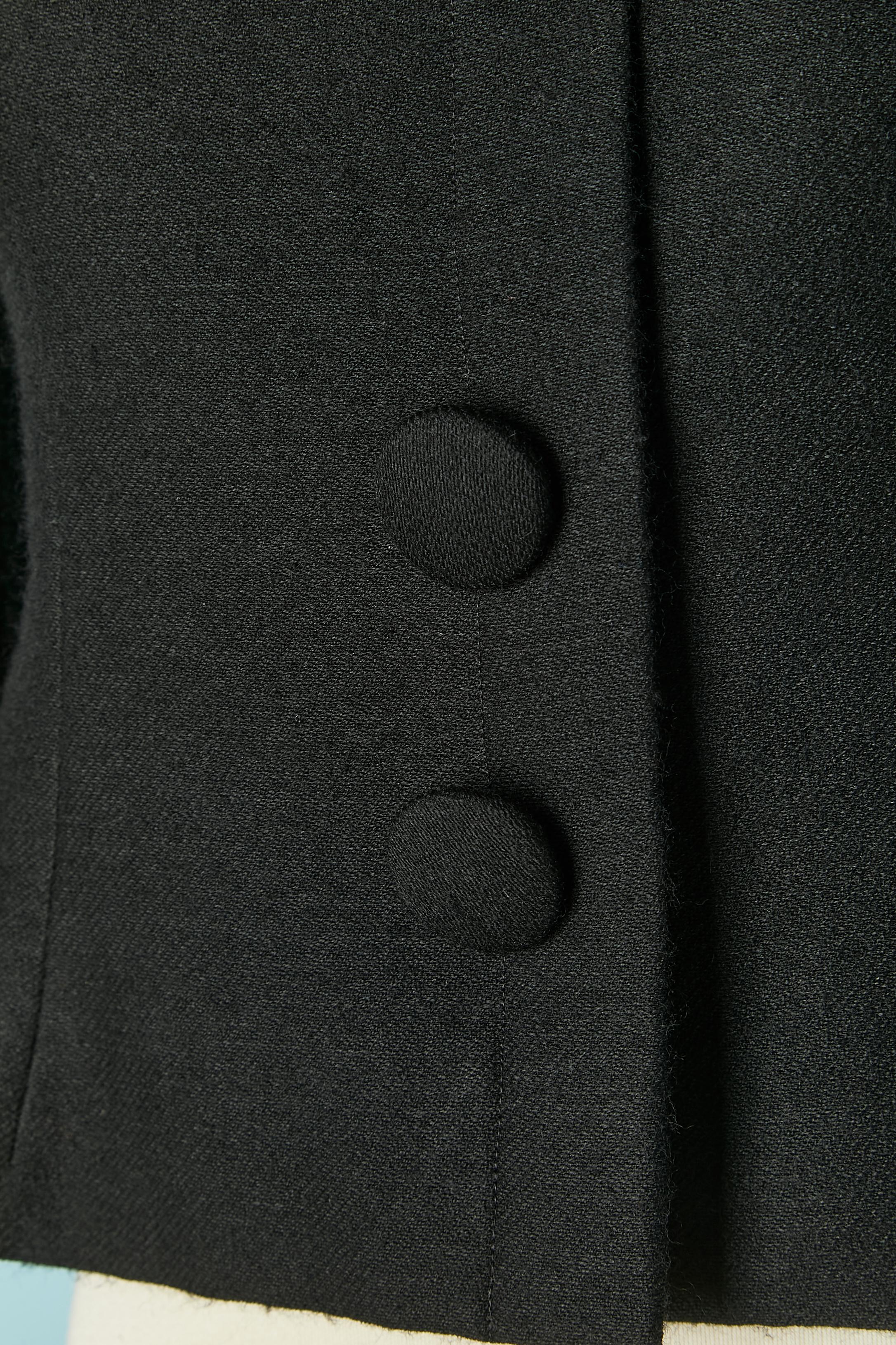 Chaqueta de lana negra con pajarita. El forro probablemente sea de rayón o acetato. Cierre a presión oculto en la parte delantera central con botón decorativo en la parte superior. 
TALLA 38/ M 