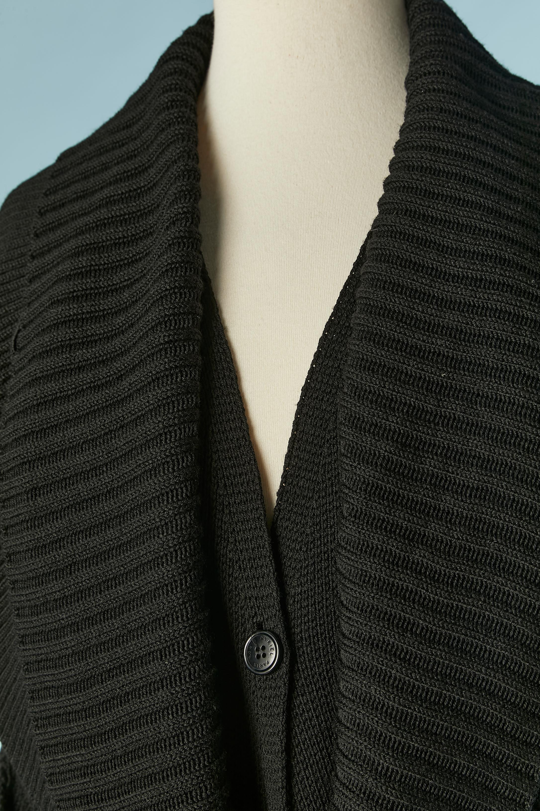 Manteau en maille de laine noire  avec ceinture en tricot. Boutons de marque. Col double épaisseur et broche de marque sur le haut du col à gauche. 
Taille S sur l'étiquette mais taille M