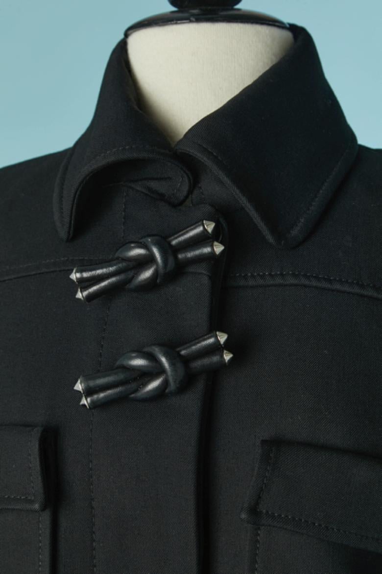 Manteau en laine noire avec noeud en cuir. Composition du tissu : 99% laine, 1% soie. Doublure en rayonne. Bouton caché et fermeture à la boutonnière sur le milieu du devant. Un bouton sur la manchette. 4 poches sur le devant ( 2 sur le buste, 2 sur