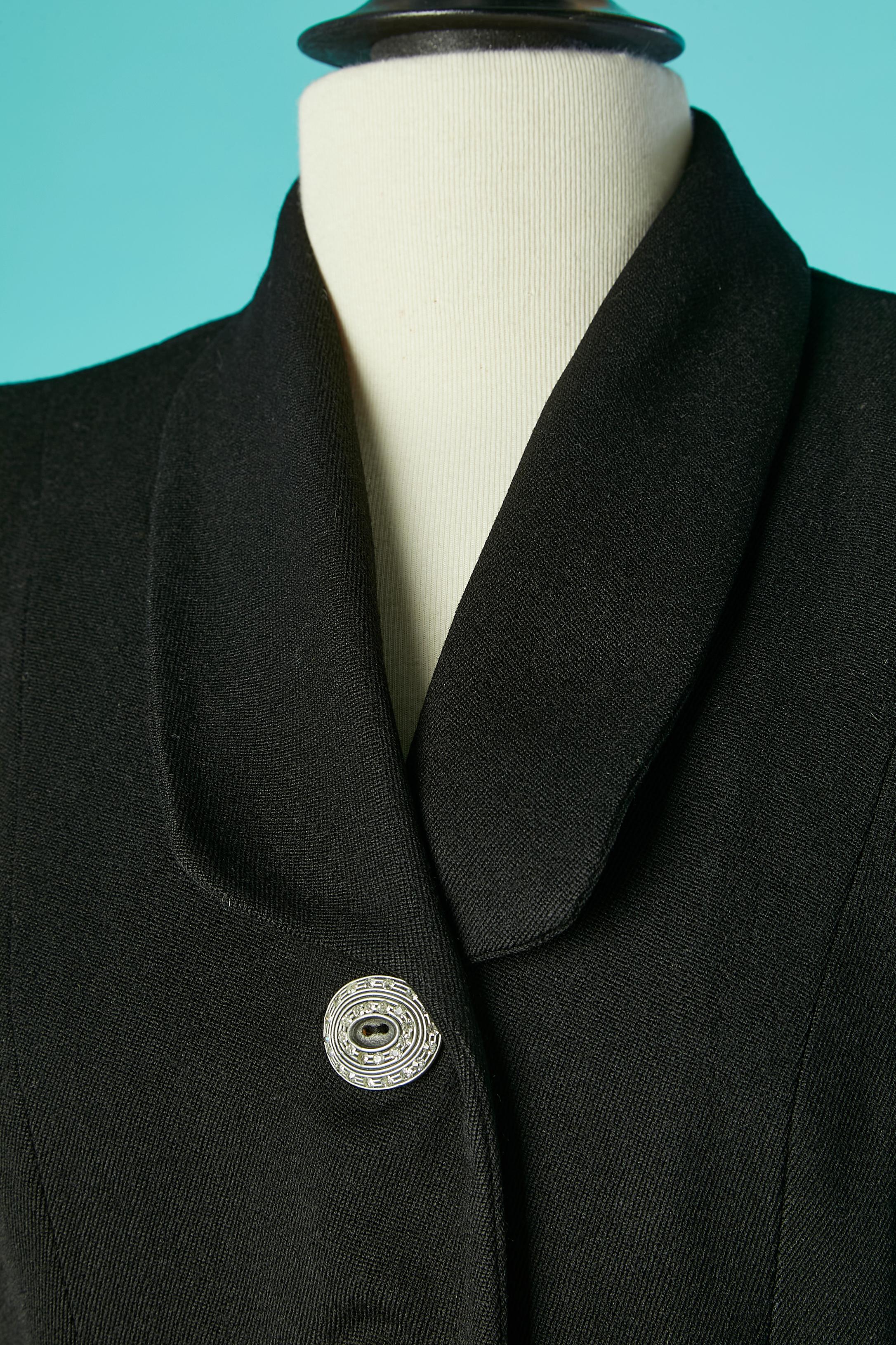 Black wool skirt-suit with jewlery  rhinestone buttons and cut-work. Rayon lining. Thick Shoulder-pads. Fake pockets. Godets on the bottom back of the jacket. Pleated satin details on the bottom of the skirt ( which could be in the back, not on the