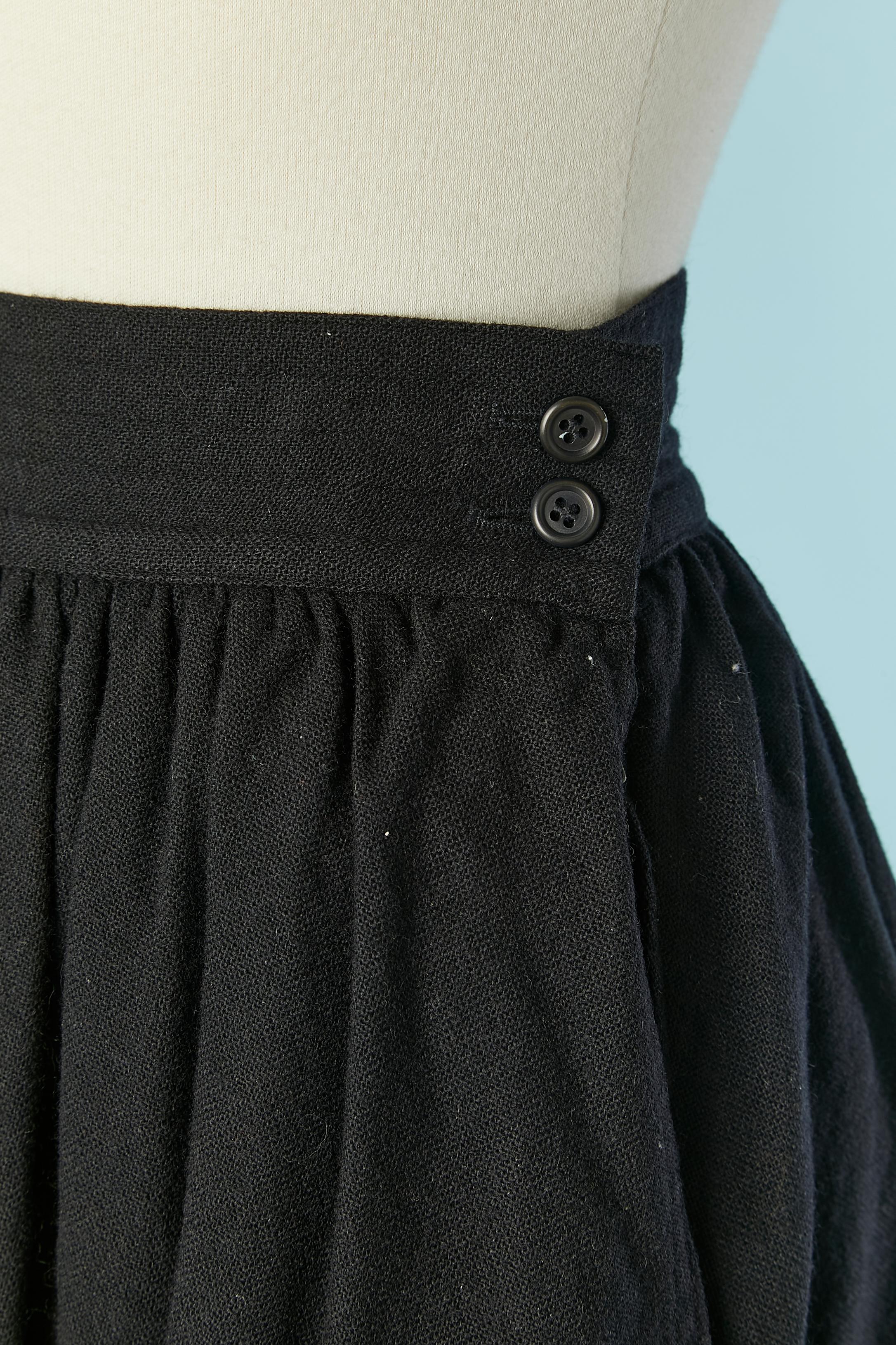 Gonna in lana nera con tasca su entrambi i lati. 
Fodera in acetato o rayon. Chiusura con bottoni, asole e zip sul lato sinistro. 
Cintura con impunture.
TAGLIA 34 / XS 