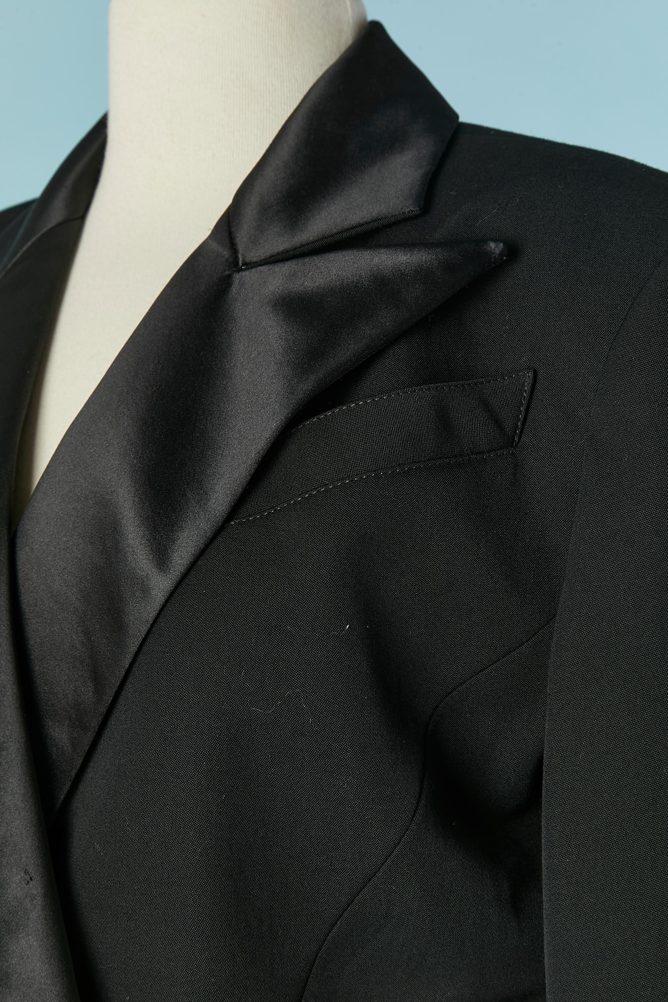 Tuxedo-Rockanzug aus schwarzer Wolle. Zusammensetzung des Hauptgewebes: Wolle . Futter (nur im Inneren der Jacke) Rayon
Druckknopfverschluss in der vorderen Mitte und an den Ärmeln. Schnittarbeiten. Schulterpolster. 
Größe der Jacke: 38 (Fr) M