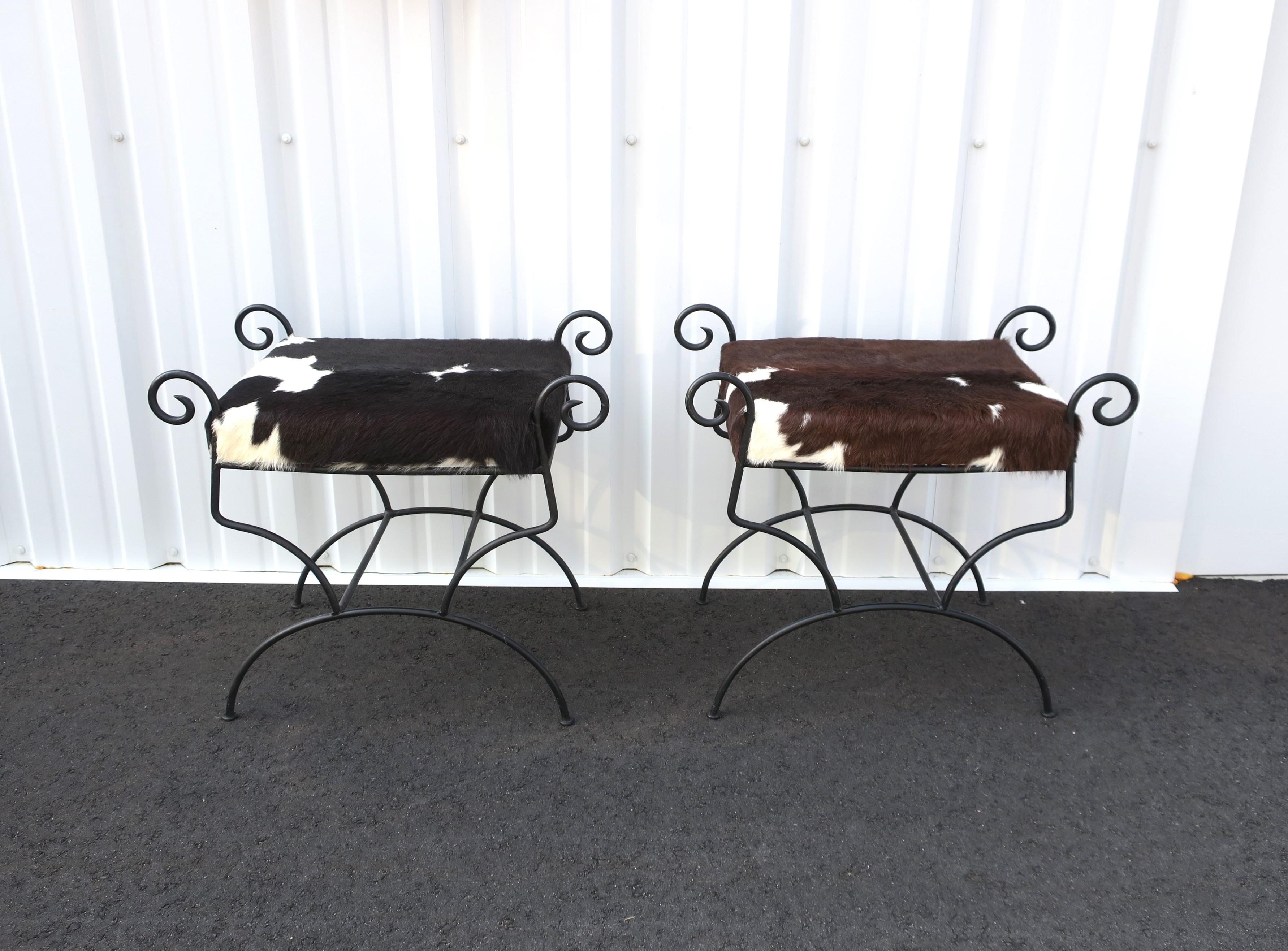 A pair/set of black wrought iron benches or stools with hide seats in the rustic design style, circa late-20th century to early 21st century. Hide seat cushions appear to be newly upholstered. Each of the hide seats are comfortable and firm, one