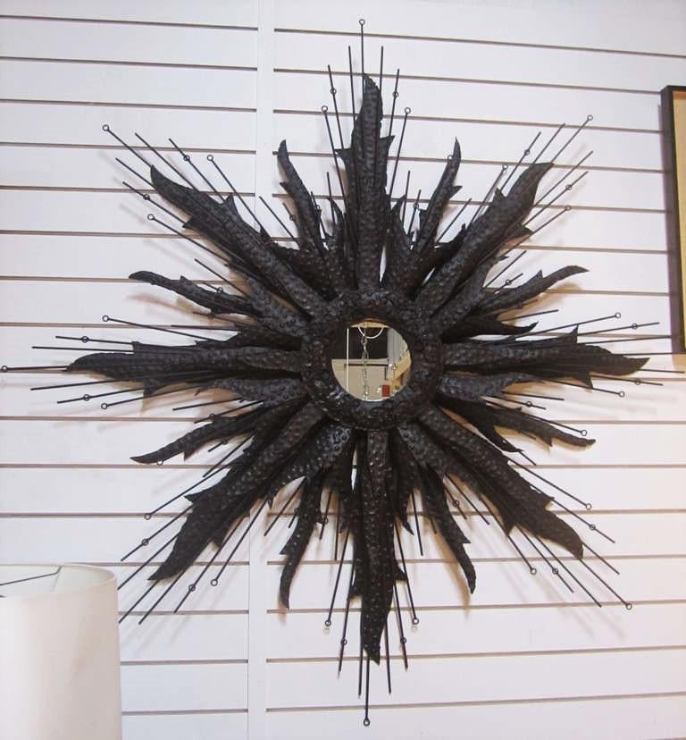 American, mid-20th century. Blackened Brutalist style polychromed steel wall-hanging starburst mirror, with a central, round mirrored panel, bordered with shaped wire scrolls, surrounded by hammered torch-cut sunrays and wire rods.