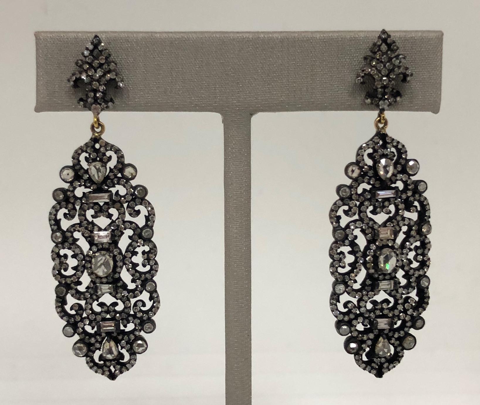 The blackened gold pendant style earrings are set with rustic, light brown, included, single, baguette and rose cut diamonds; the top is formed in the figure of a diamond set flour-de-lis, with ornate curved and swirled damask-style patterned