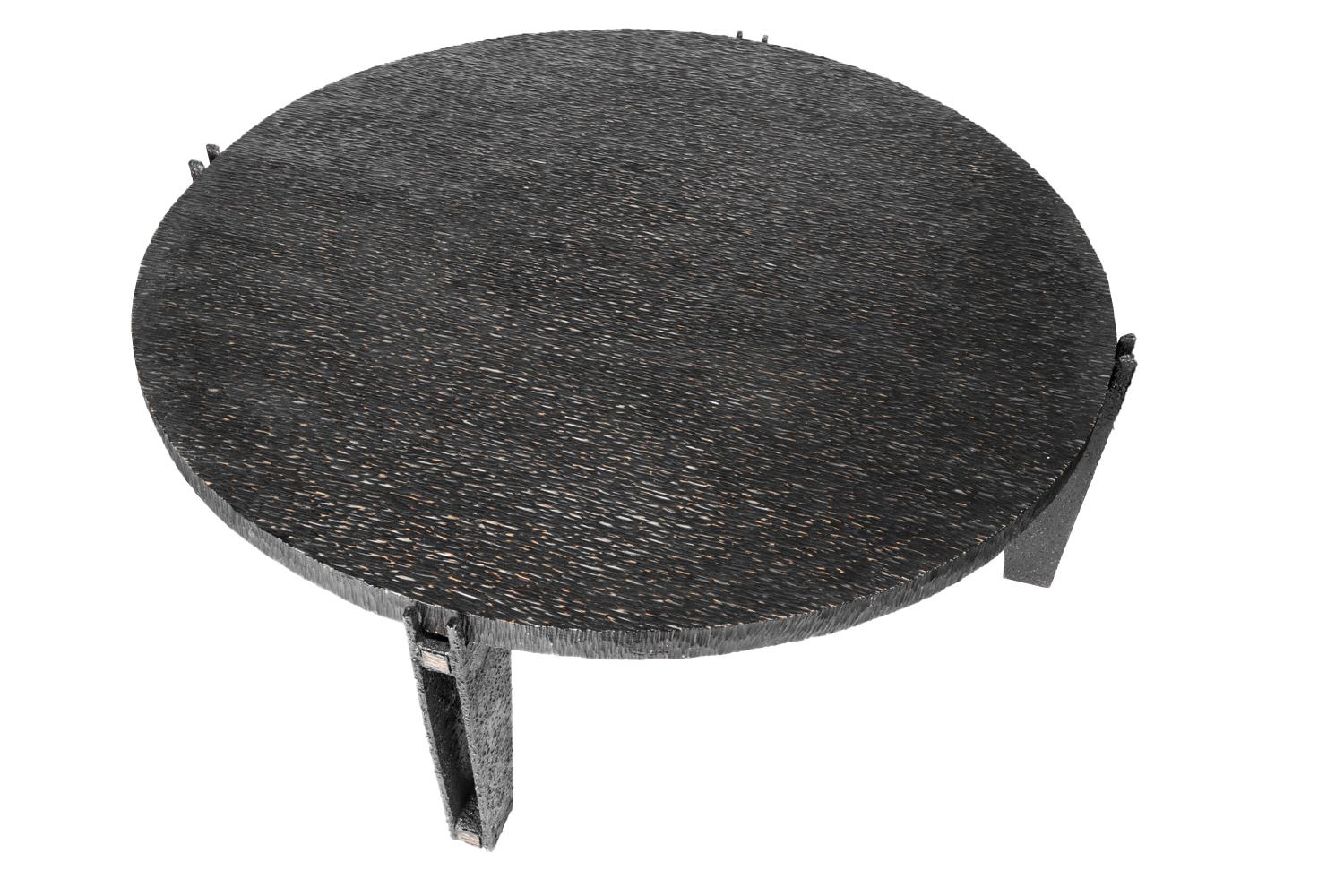 Round coffee table standing on four tapered legs in rectangular black metal, opened in their center.
They support a circular tray in blackened gouged wood forming sort of waves.

French contemporary work.

The gouged wood is a technique of wood