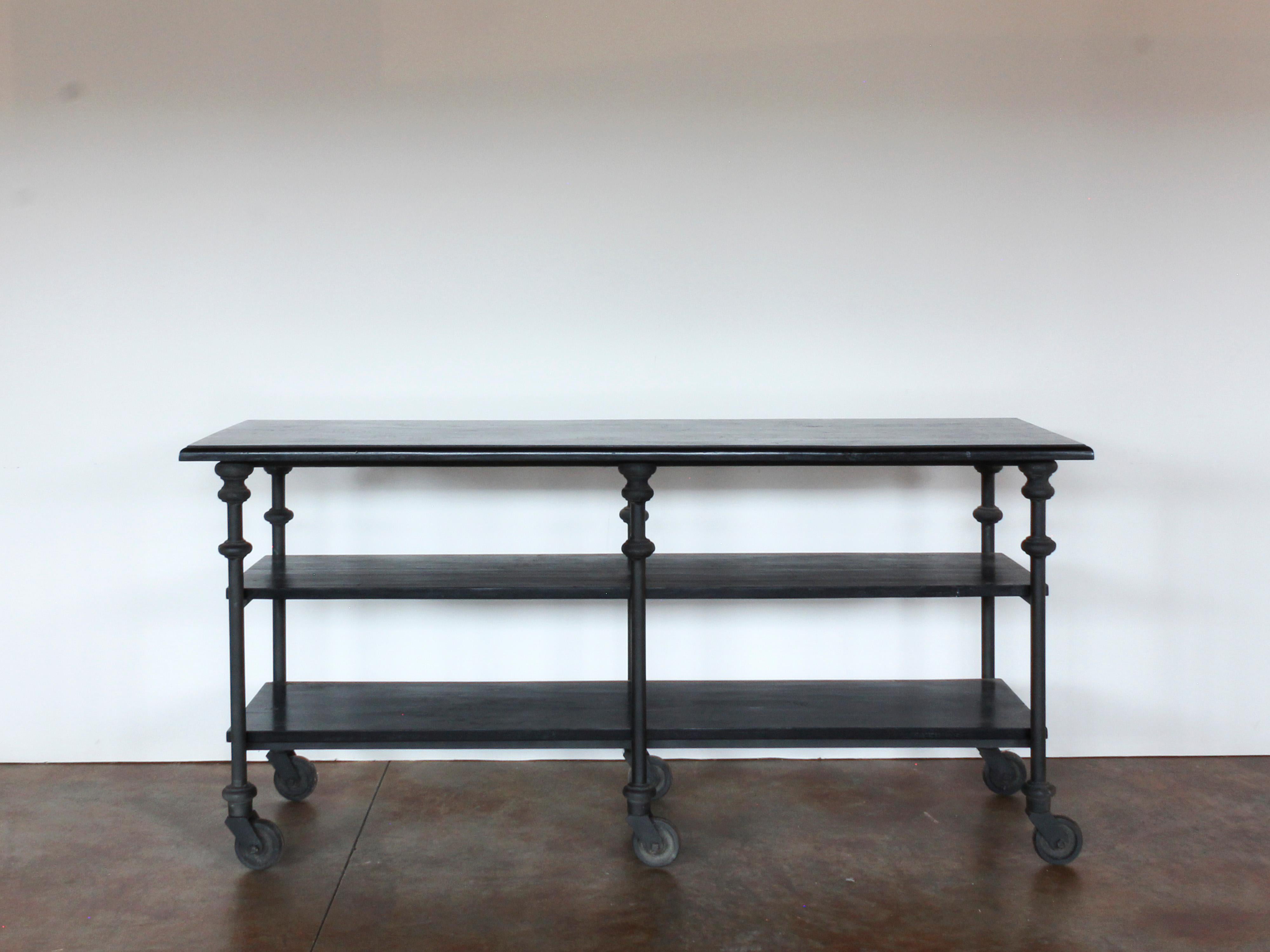 Industrial style blackened wood and iron three-tier shelving unit or island on casters. Sits on six (6) casters/wheels. Two (2) available.