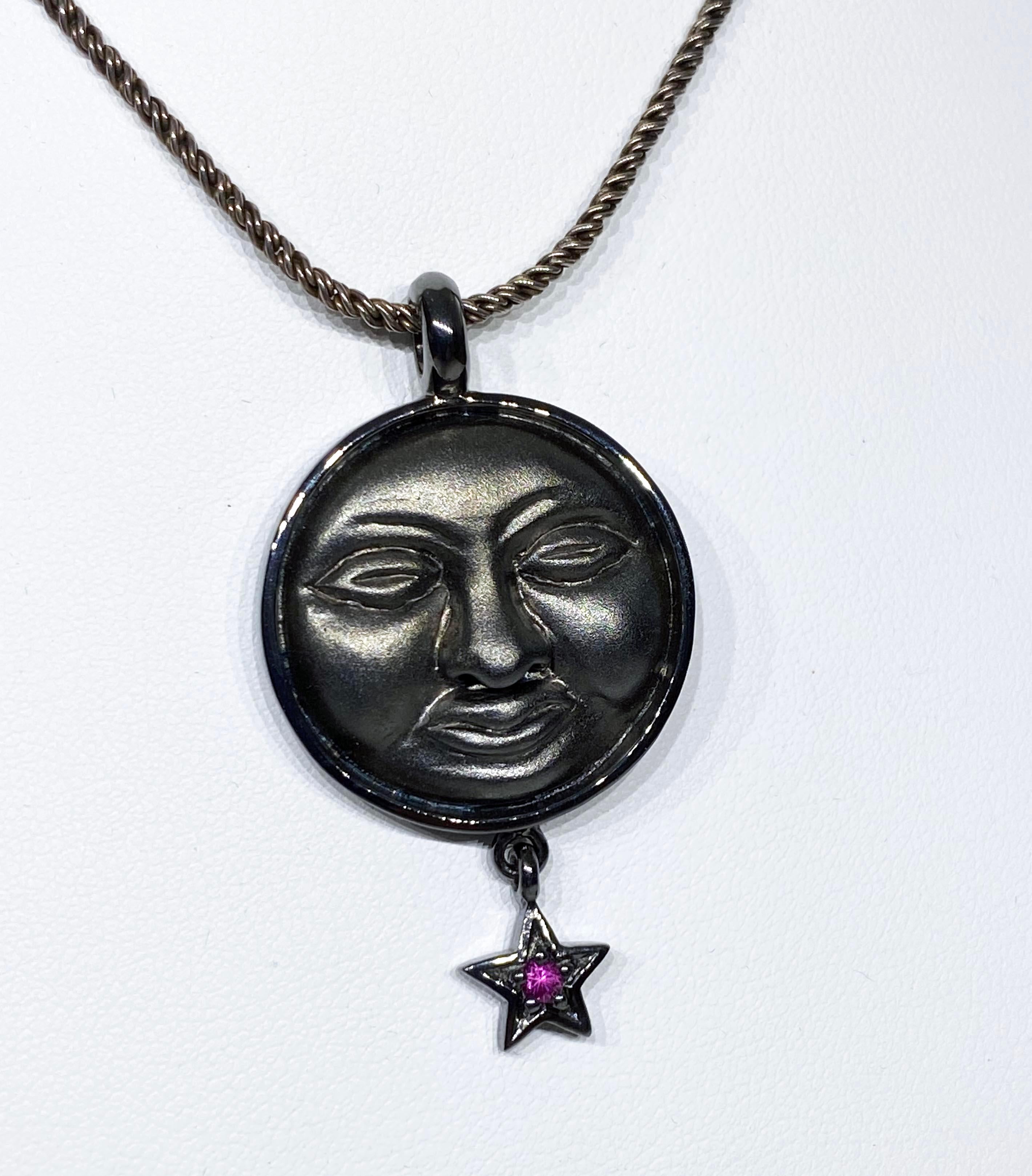 A Blackened Silver Moon Face Pendant
This Blackened Silver Moonface Pendant is is 1.75 inches long and 1 inch wide, This Pendant Slides on a Blackened Silver Chain of 17 Inches. It is acented by a small star dangle set with a Pink Sapphire Round of
