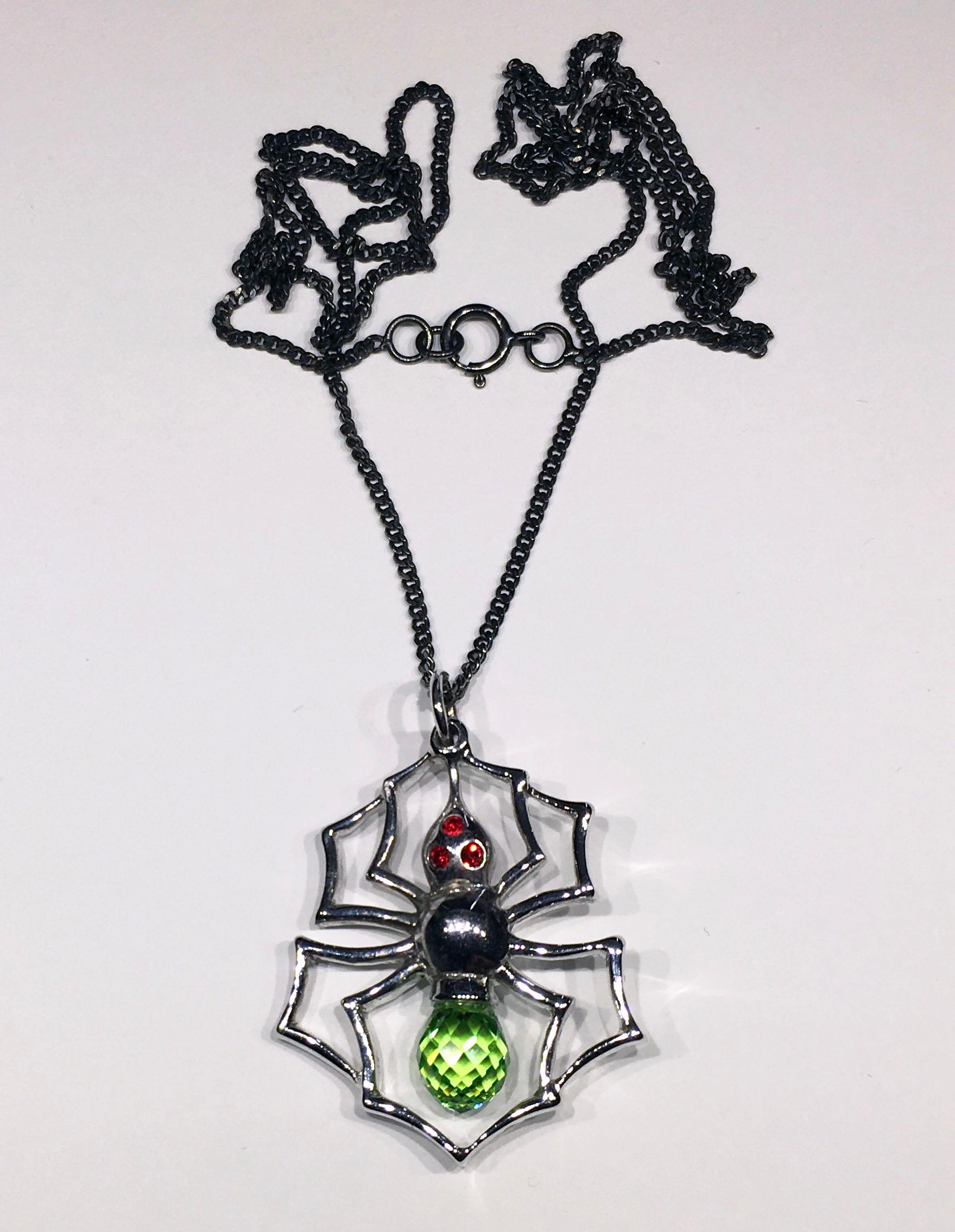 Kary Adam Designed, A Blackened Silver Spider Pendant with Cultured Green Sapphire Body, & Red Zirconia Eyes. This Pendant is hung from a Blackened Silver Chain of 20