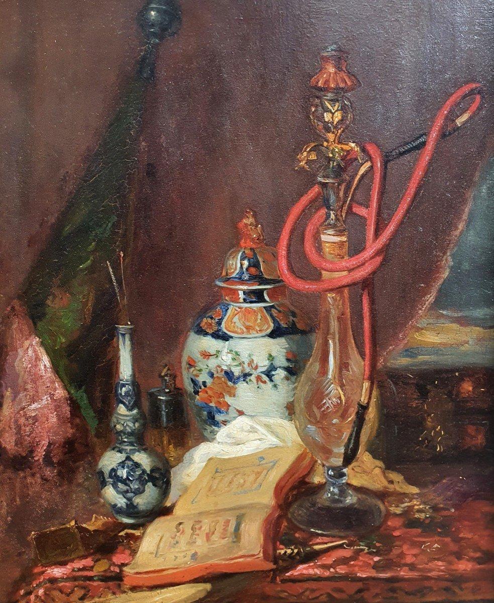 Blaise Alexandre Desgoffe's oil on panel is a captivating representation of Orientalist allure combined with meticulous detail. The central focus, a gracefully curved hookah, is surrounded by Chinese ceramics and an eloquently bound book, hinting at