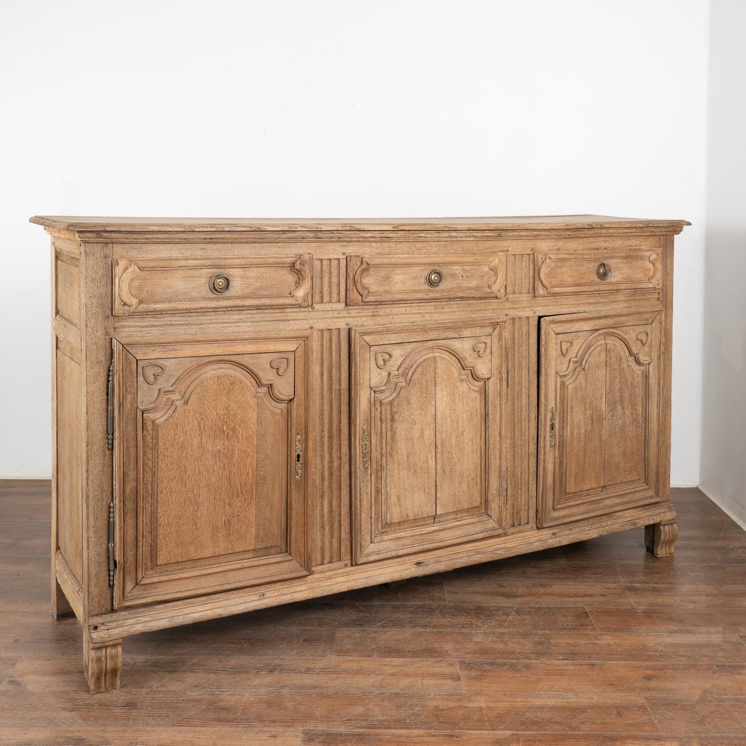 It is the lovely carved details and heavily paneled drawers and doors that draws one to this French oak sideboard which has been bleached giving it a lighter finish for today's modern home.
The panel doors are accented with two small hearts in the