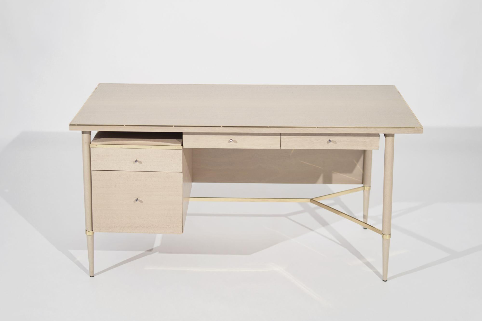 Introducing the Bleached Mahogany Desk from Paul McCobb's Connoisseur Collection, meticulously restored by Stamford Modern. Crafted in the 1950s, this mid-century icon boasts minimalistic lines, sleek silhouette, and bleached mahogany warmth. Brass