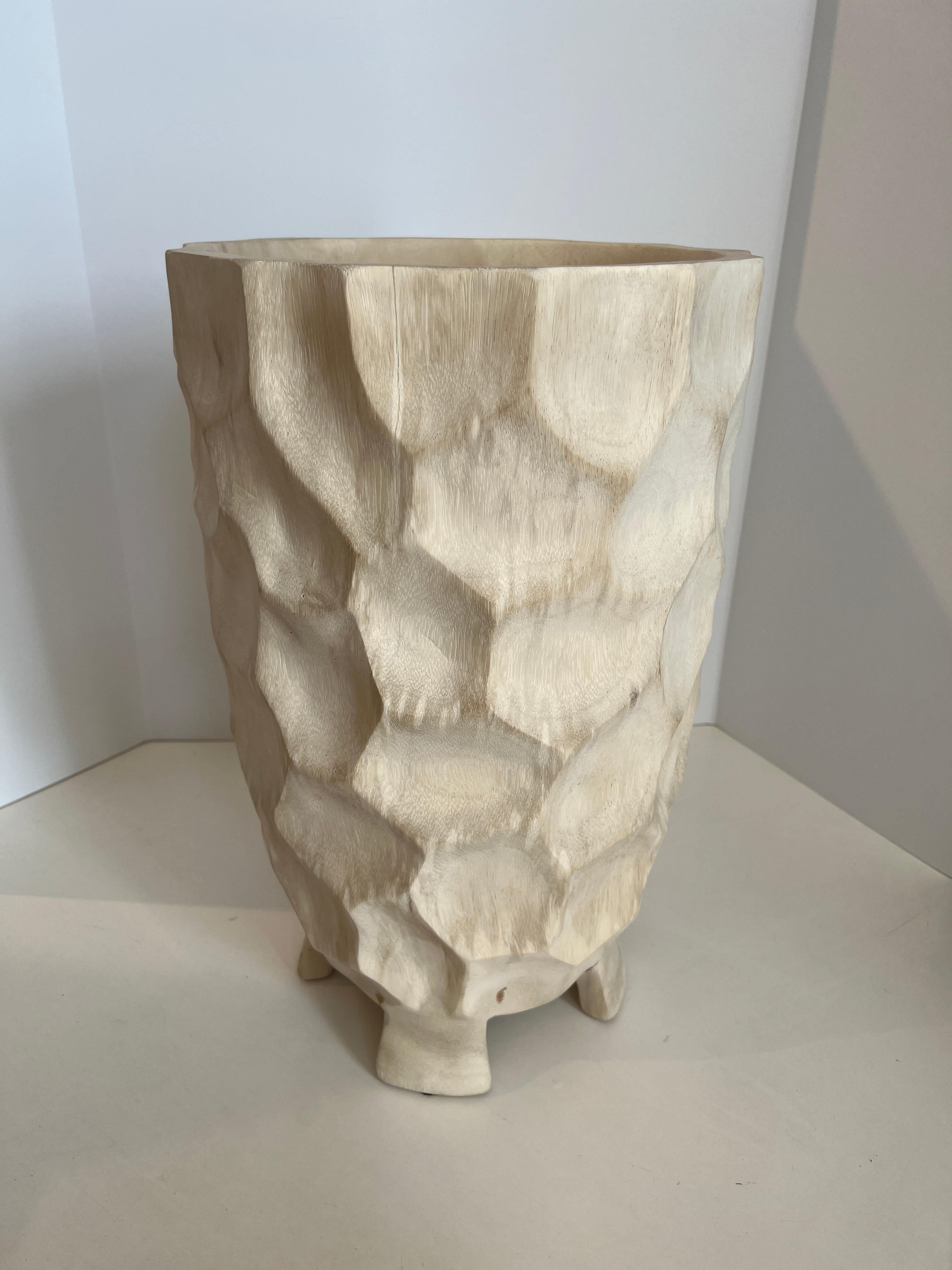 Tall wooden vase with hand carved mottled surface the creates light and shadow. Perched on four feet.