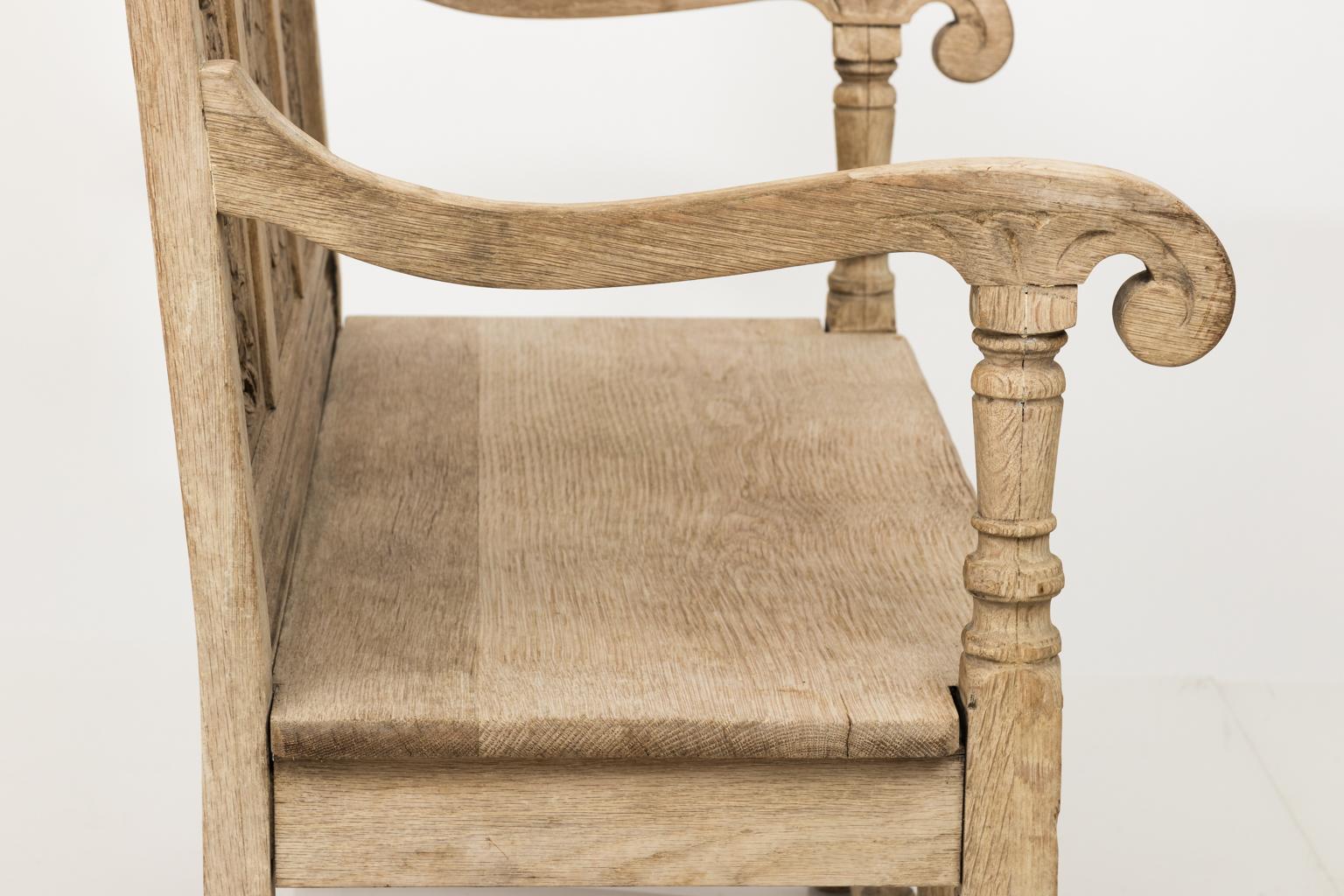 Heavily carved American made Jacobean style bench in bleached oak that features foliaged shallow relief carvings on three-seat back panels, scrolled arms, and bulb turned legs, circa 1902.