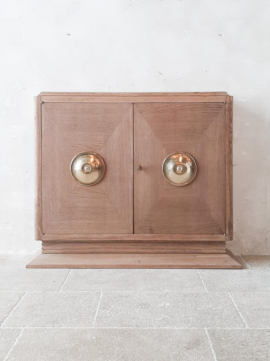 Bleached oak credenza by Charles Dudouyt from the 1940s. Midcentury Art Deco style sideboard with a large round brass detail on the middle of the doors.

Measures: H 101 x W 115 x D 31 cm.

Good condition, wear consistance with age and use, few