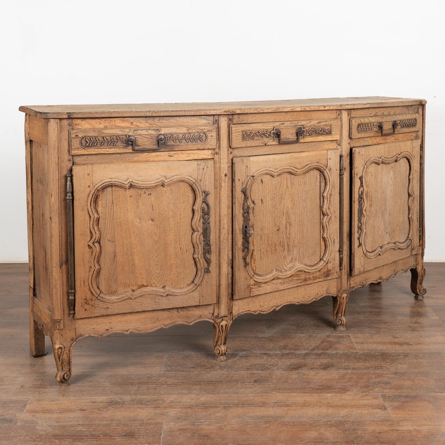 6' long French bleached oak sideboard with unique convex/bow front, traditional carved panel doors and carved vine details along 3 drawers.
This lovely oak buffet rests on carved cabriolet feet.
Middle cabinet door has a key and does lock. End doors