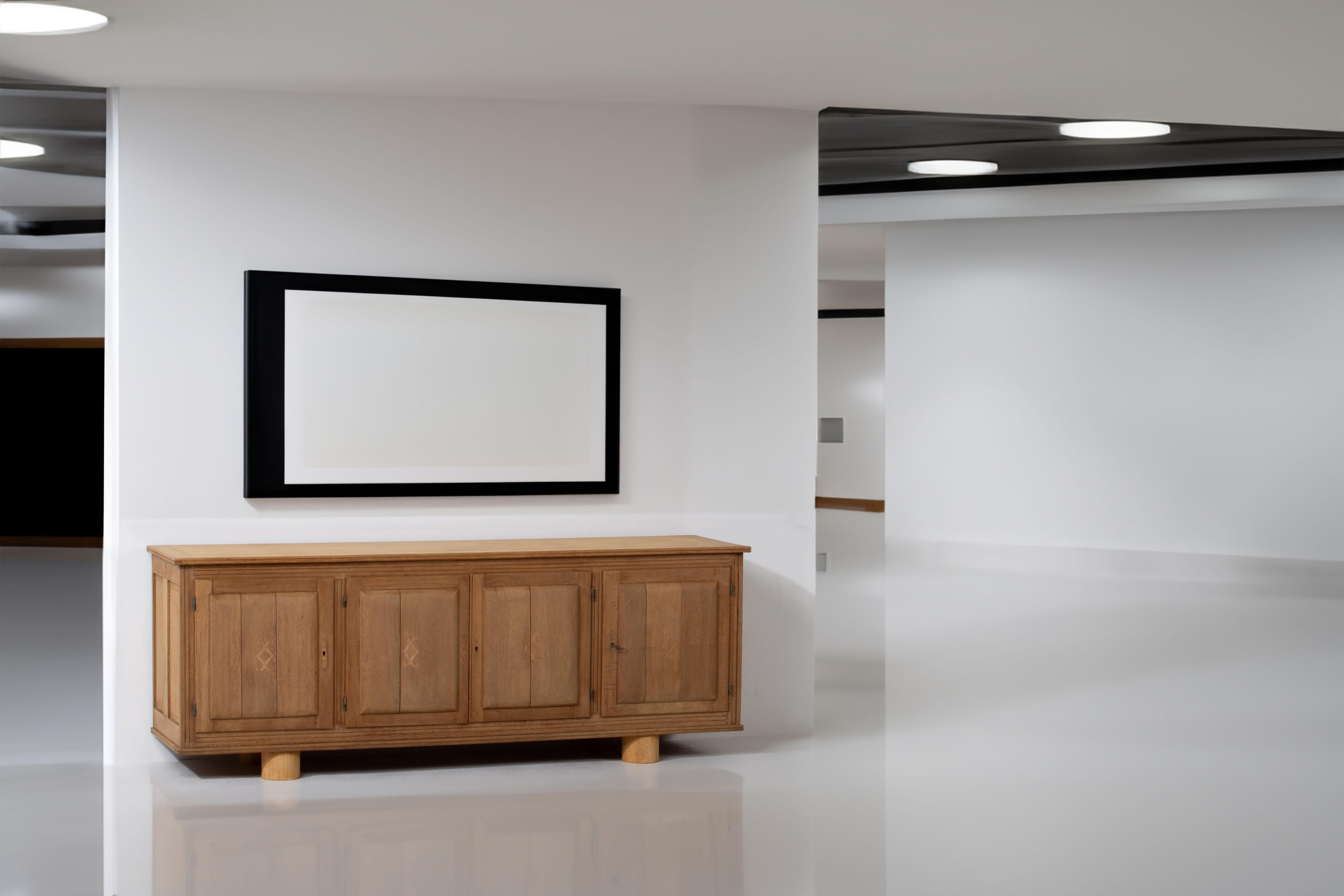 Introducing an alluring low sideboard, meticulously crafted from bleached oak and graced with plinth legs, embodying the distinct design essence of the 1950s. This sideboard harmoniously marries form and function, capturing the refined aesthetics of