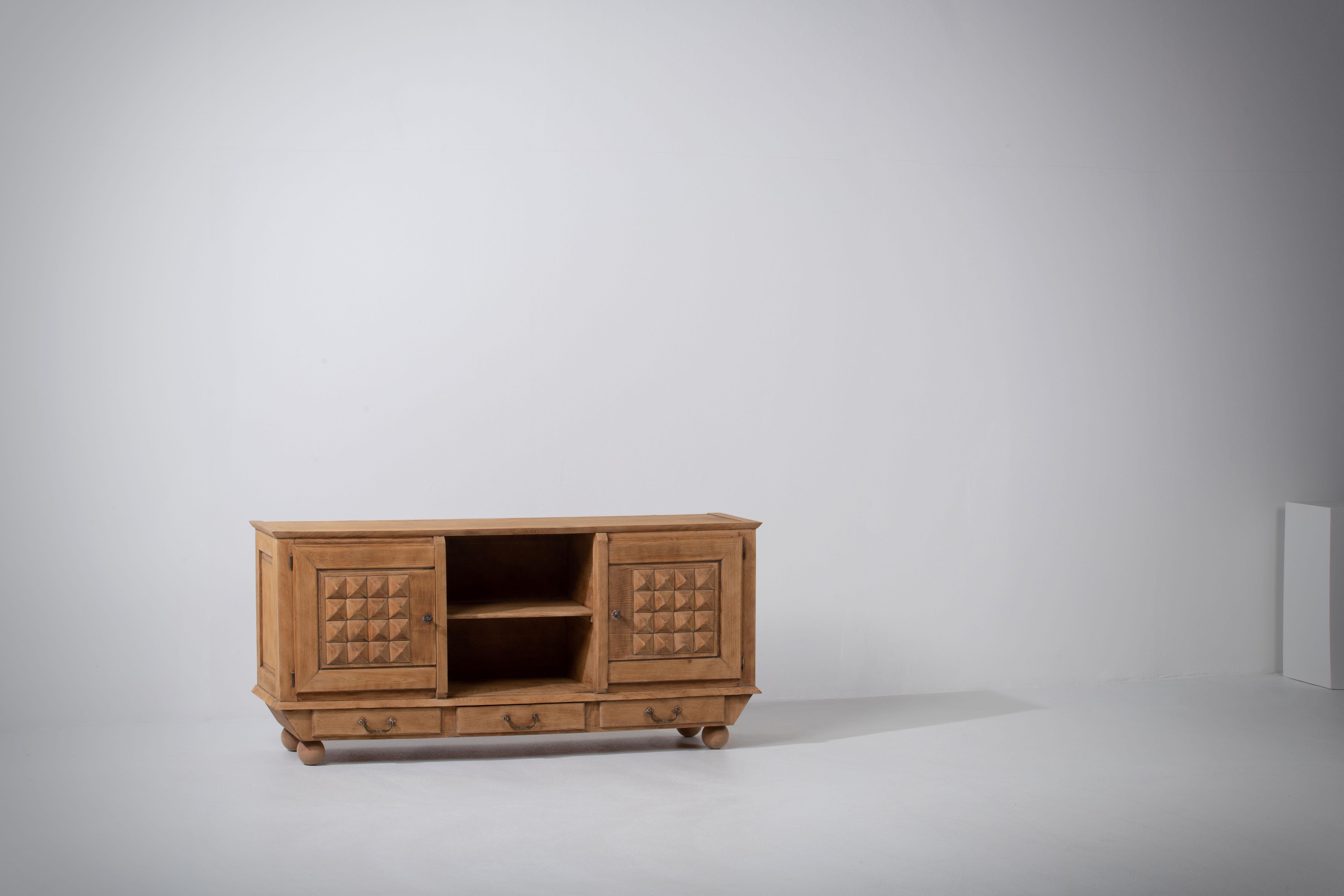 Bleached Credenza in solid oak, France, reminiscent of the work of Charles Dudouyt, 1940s.
Large Art Deco Brutalist sideboard. 
The credenza consists of two storage facilities and covered with very detailed designed doors, in the center three