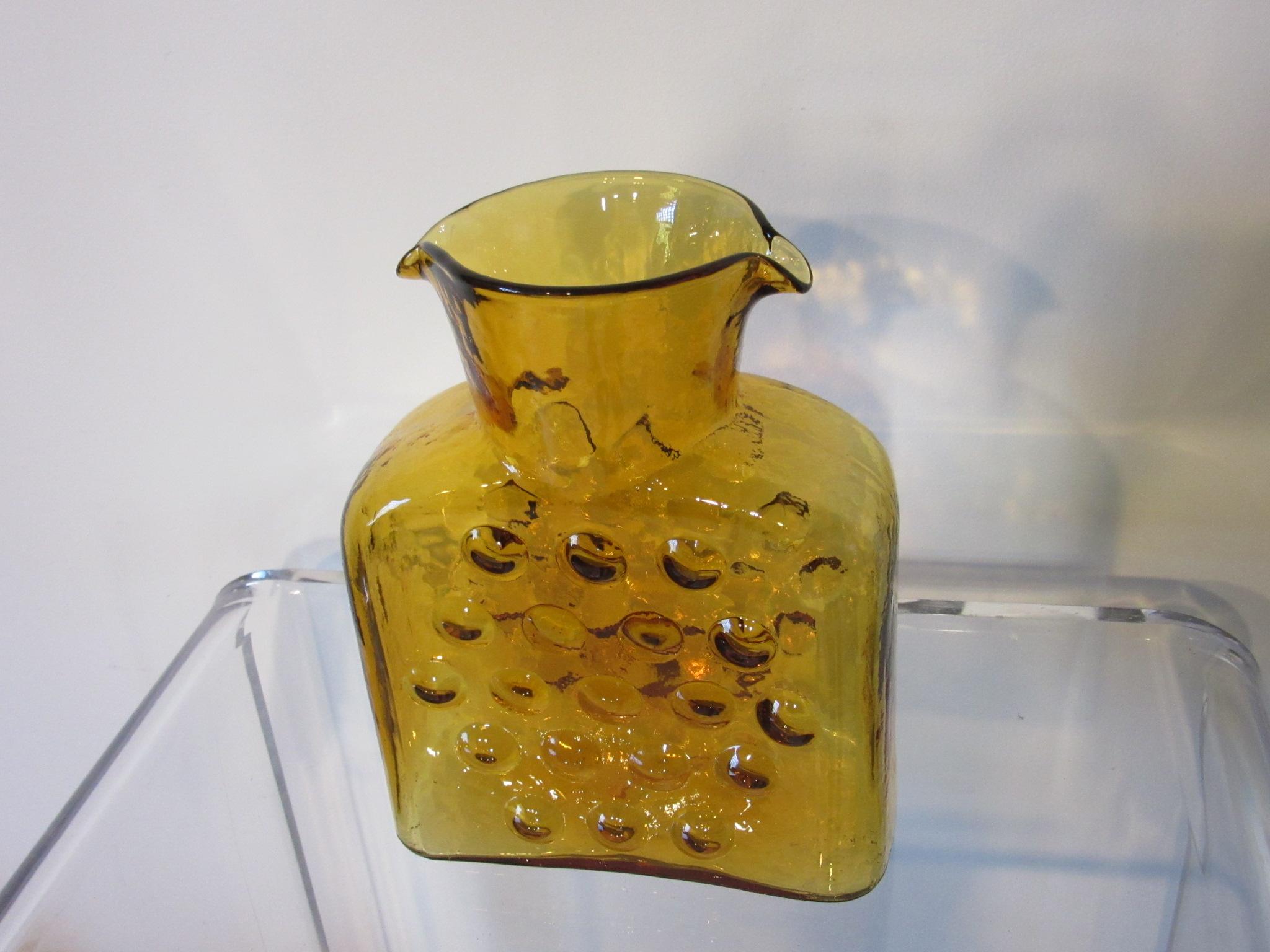 A amber hand blown glass water vessel with round bubble designs manufactured by the Blenko Glass Company .  