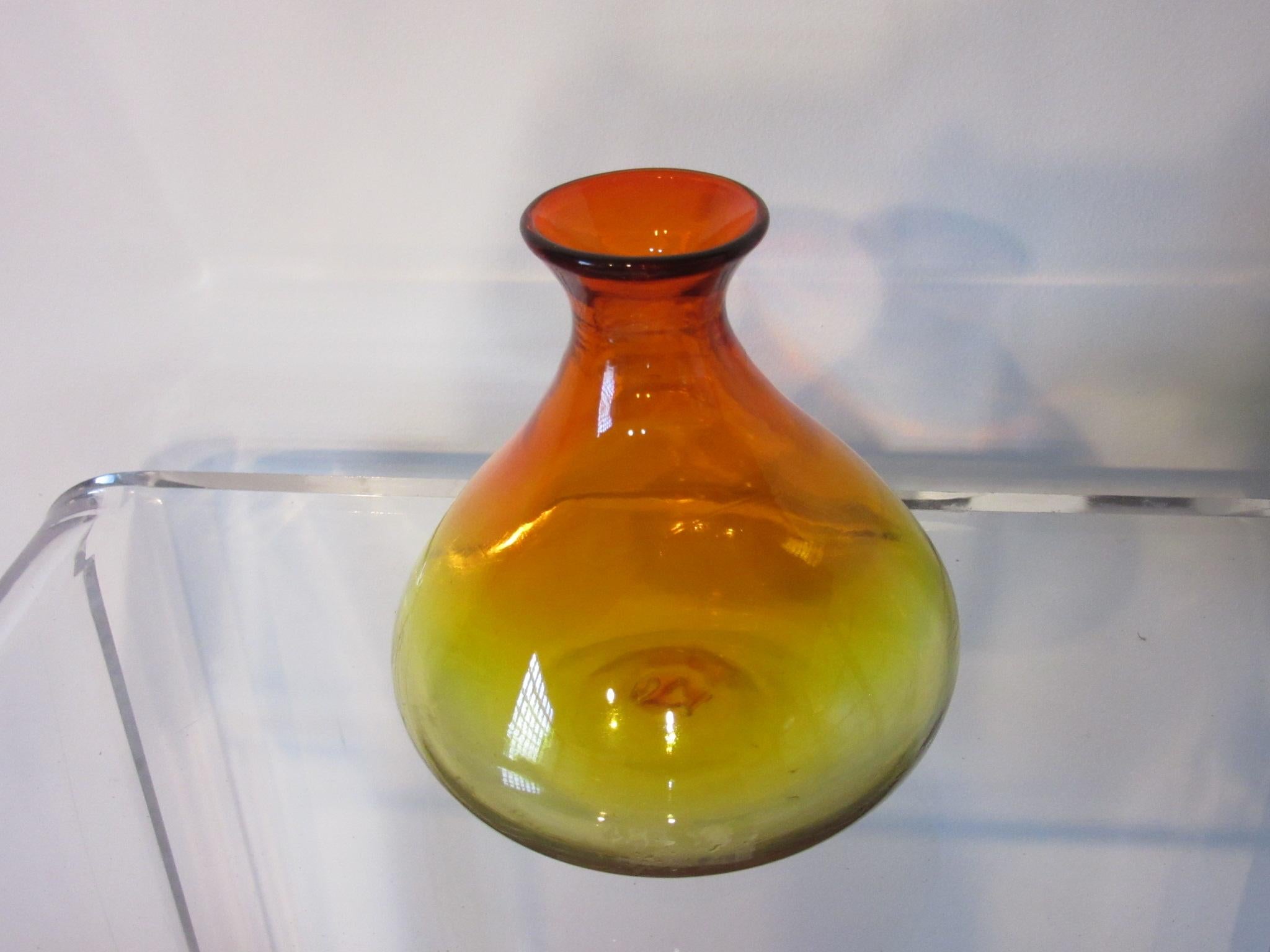 A smaller hand blown glass vase in amber with upper red highlights manufactured by the Blenko Glass company and crafted by Joel Meyer .