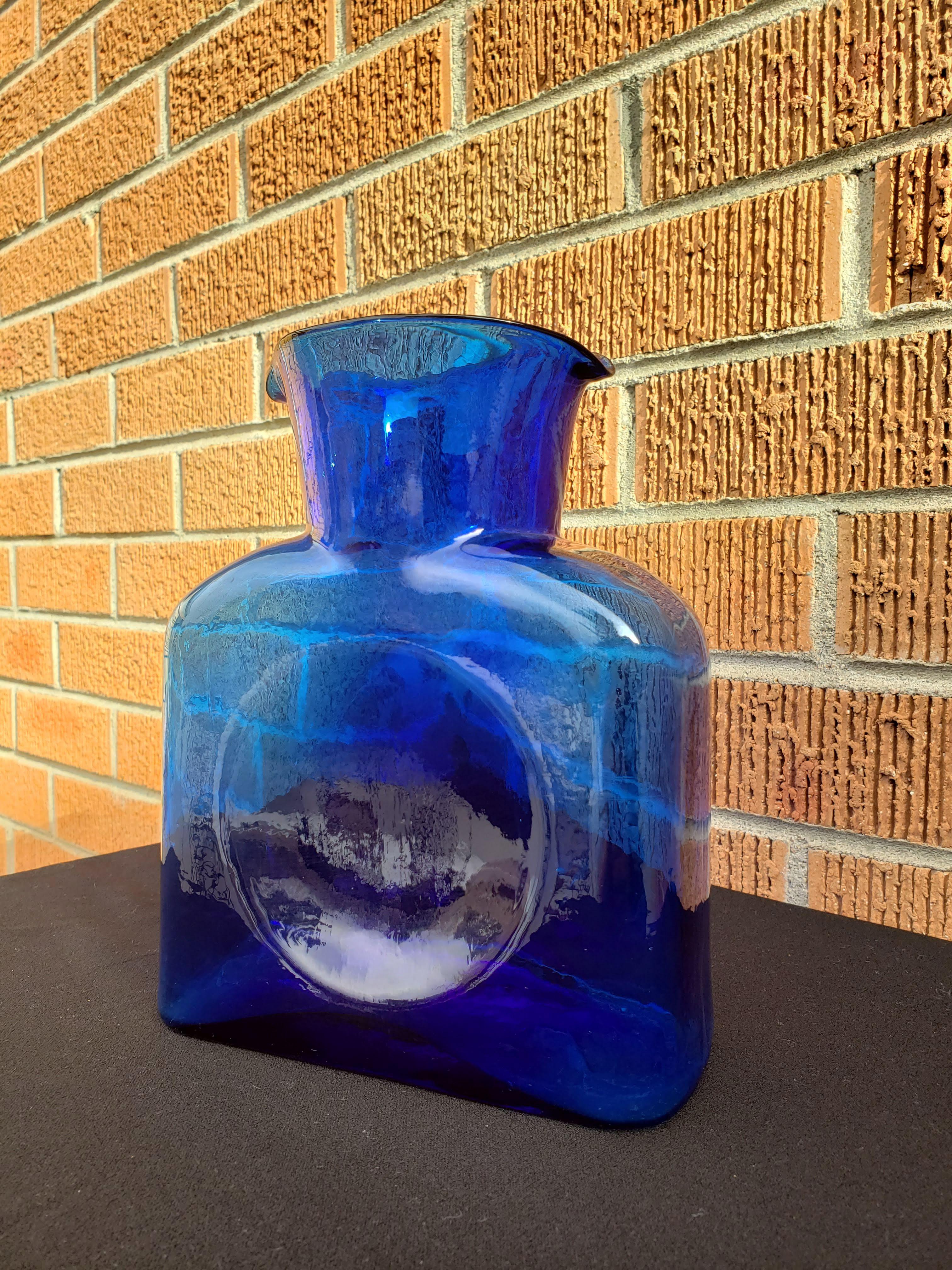 Fabulous cobalt blue Blenko iconic water bottle with sandblasted etching on base with the maker, Blenko, and the year 2002. Would be great as a vase with white peonies or in a window to catch the light.
