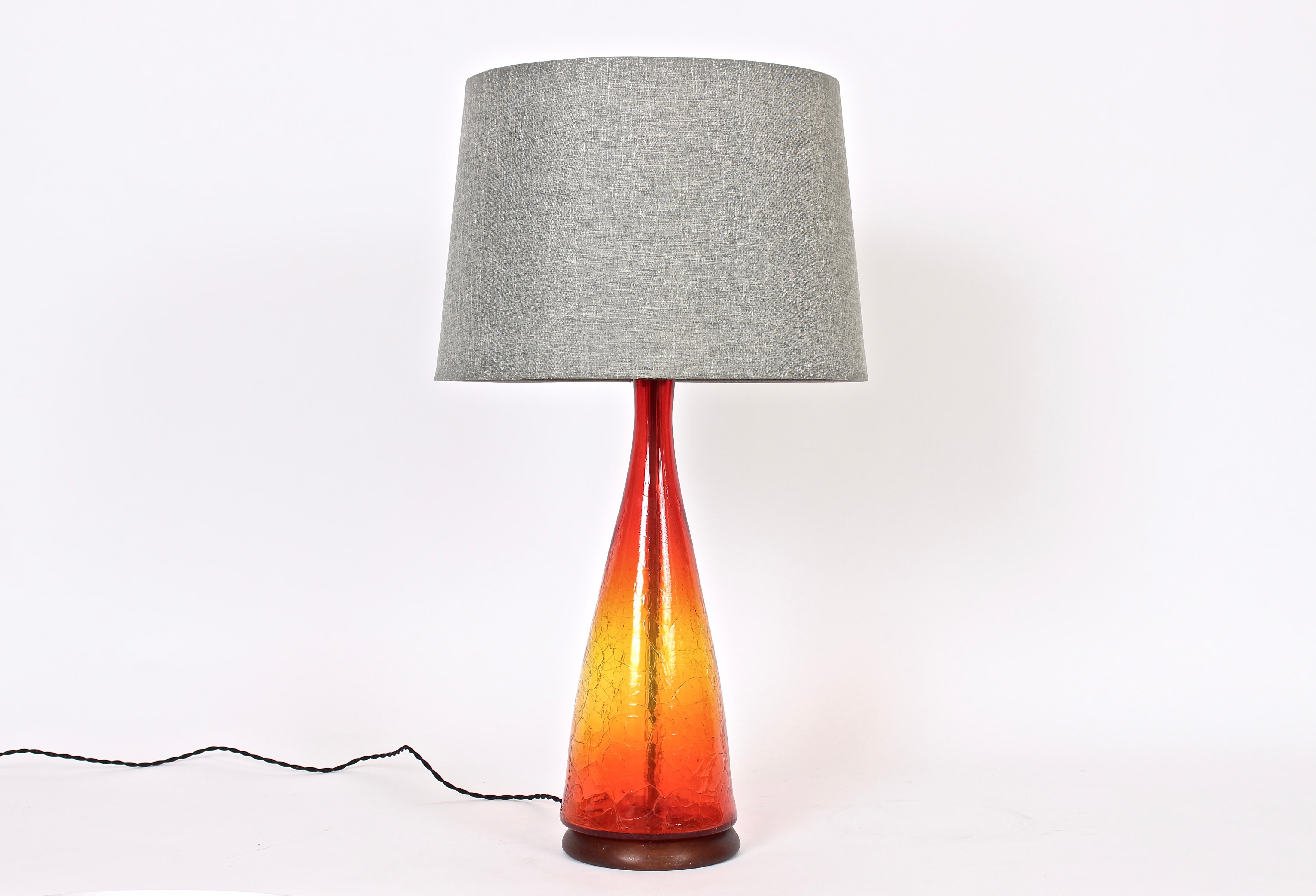 American mid century hand blown crackle glass lamp by Blenko glass company. Featuring a classic decanter form in translucent crackled glass with bright red, orange and yellow sunset coloration. On rounded solid coated wooden base. Shade shown for