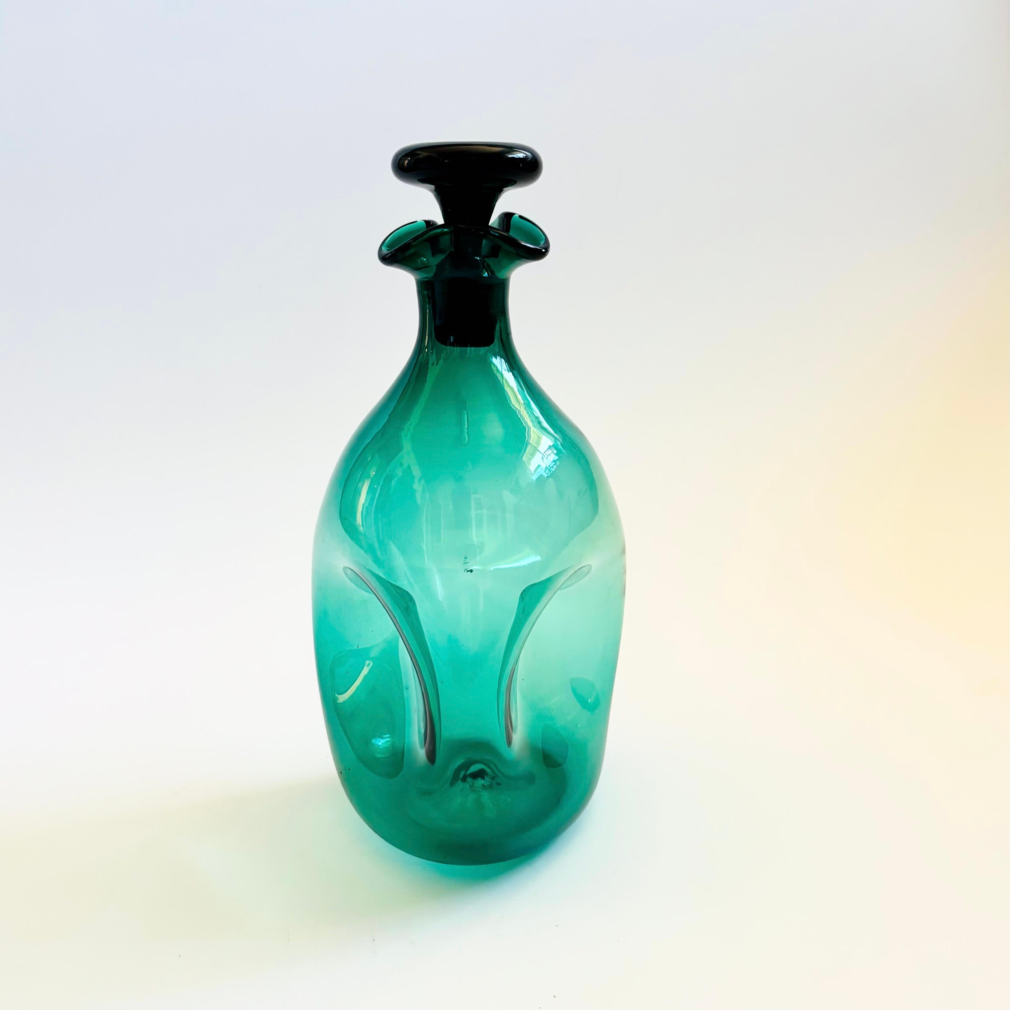 Carafe à décanter en verre pincé du milieu du siècle produite par Blenko, numéro de modèle 49. Belle couleur vert foncé du verre avec un effet pincé au centre. L'ouverture a une forme ébouriffée et est surmontée d'un bouchon plat en forme de