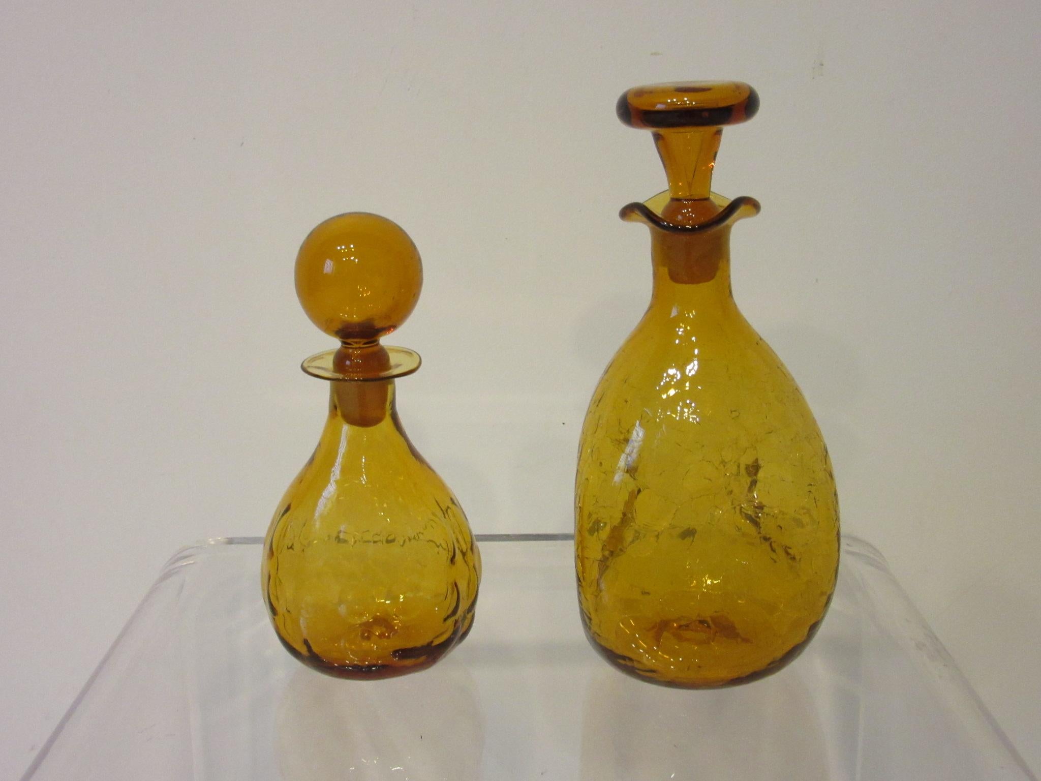 A pair of hand blown decanters with stoppers the smaller one having the bubble pattern and the larger one having the crackle pattern with pinched design. Both are in tangerine color and would work in your bar or as interior accessories make under
