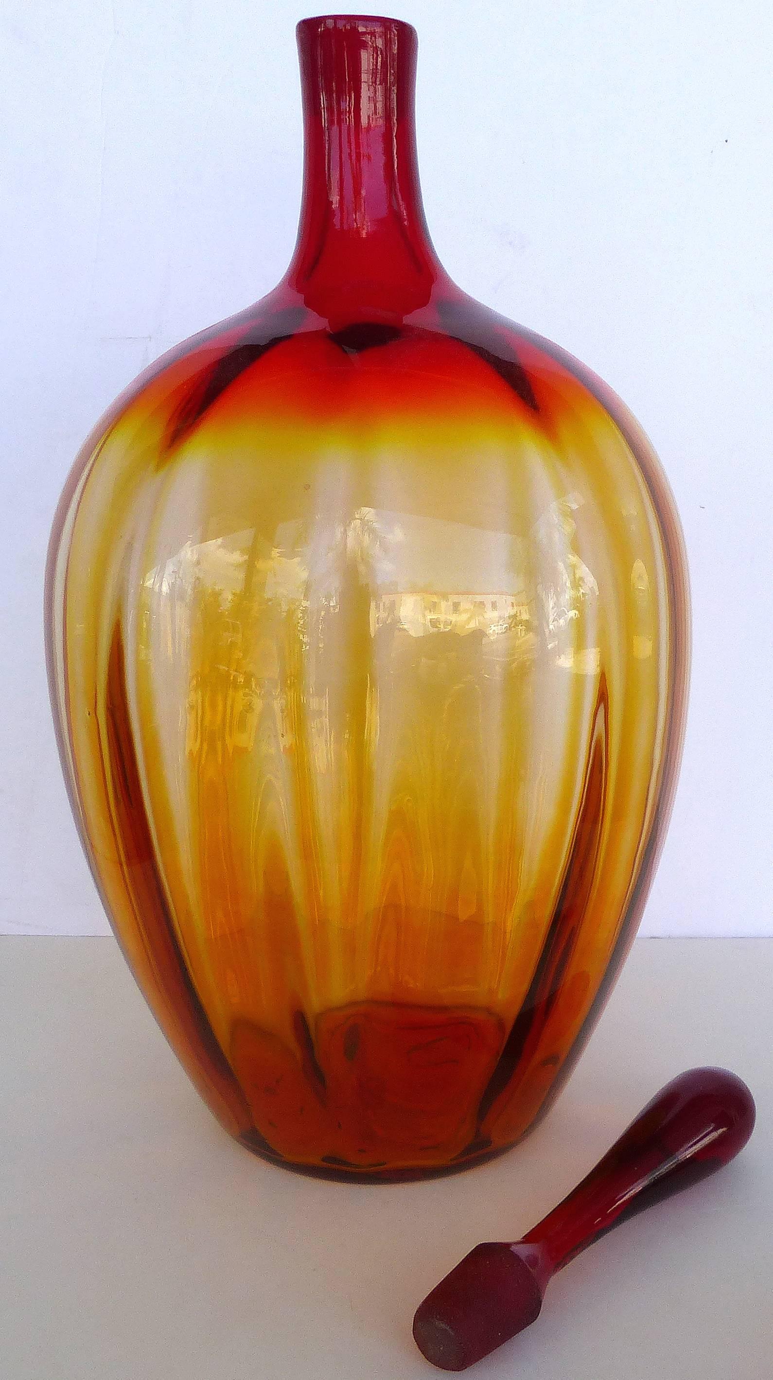 Blenko Large Decorative Bottle with Stopper

Offered for sale is a large Blenko bottle with stopper that has red to amber glass with a ribbed bulbous body. The height of the vessel without the stopper is 18