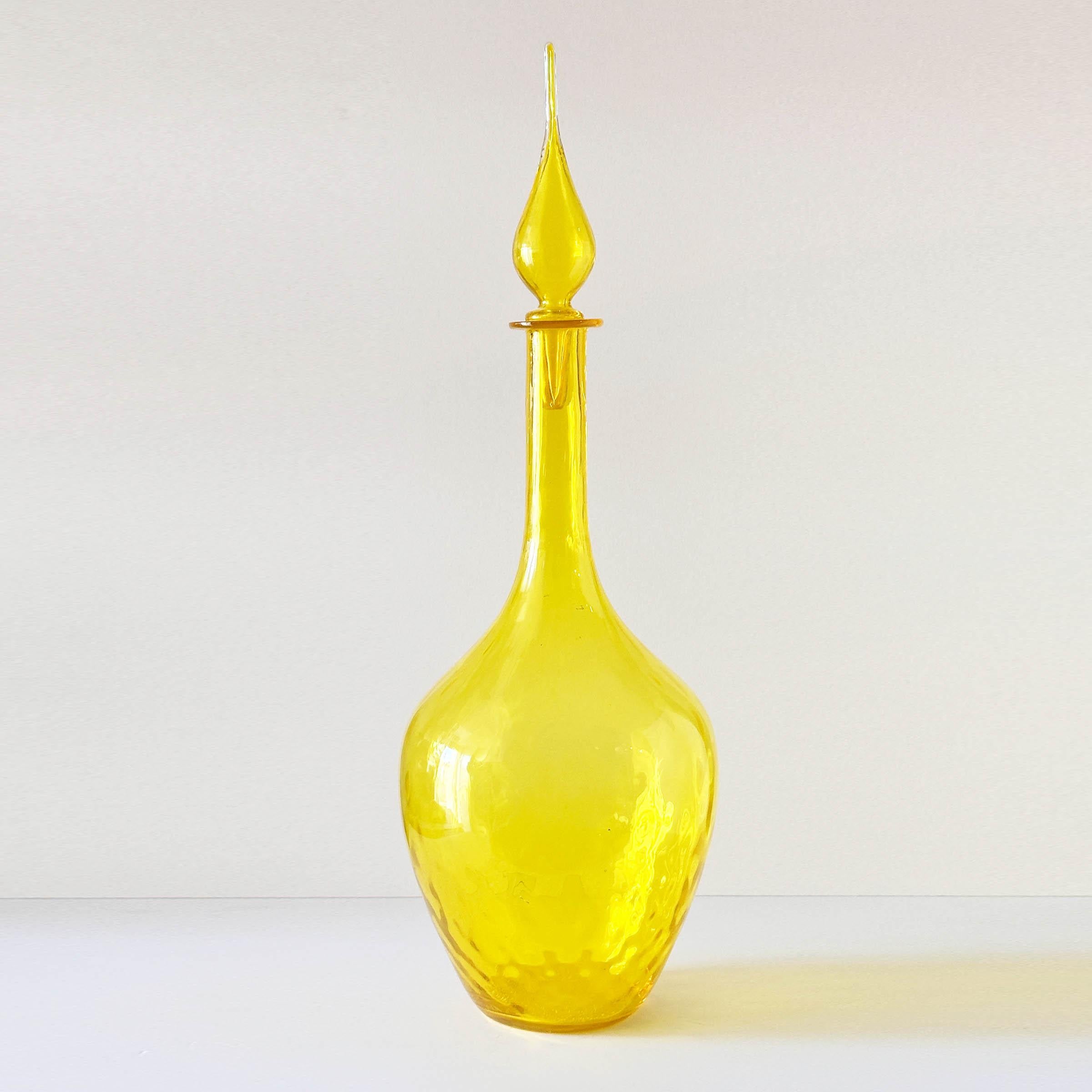 We assume this is by Blenko Glass Company however we’re still combing through their catalogs to find an exact match. It is in their popular Lemon Yellow. It has optical ribbing on the neck and optical rippling on the corpus. The total height with