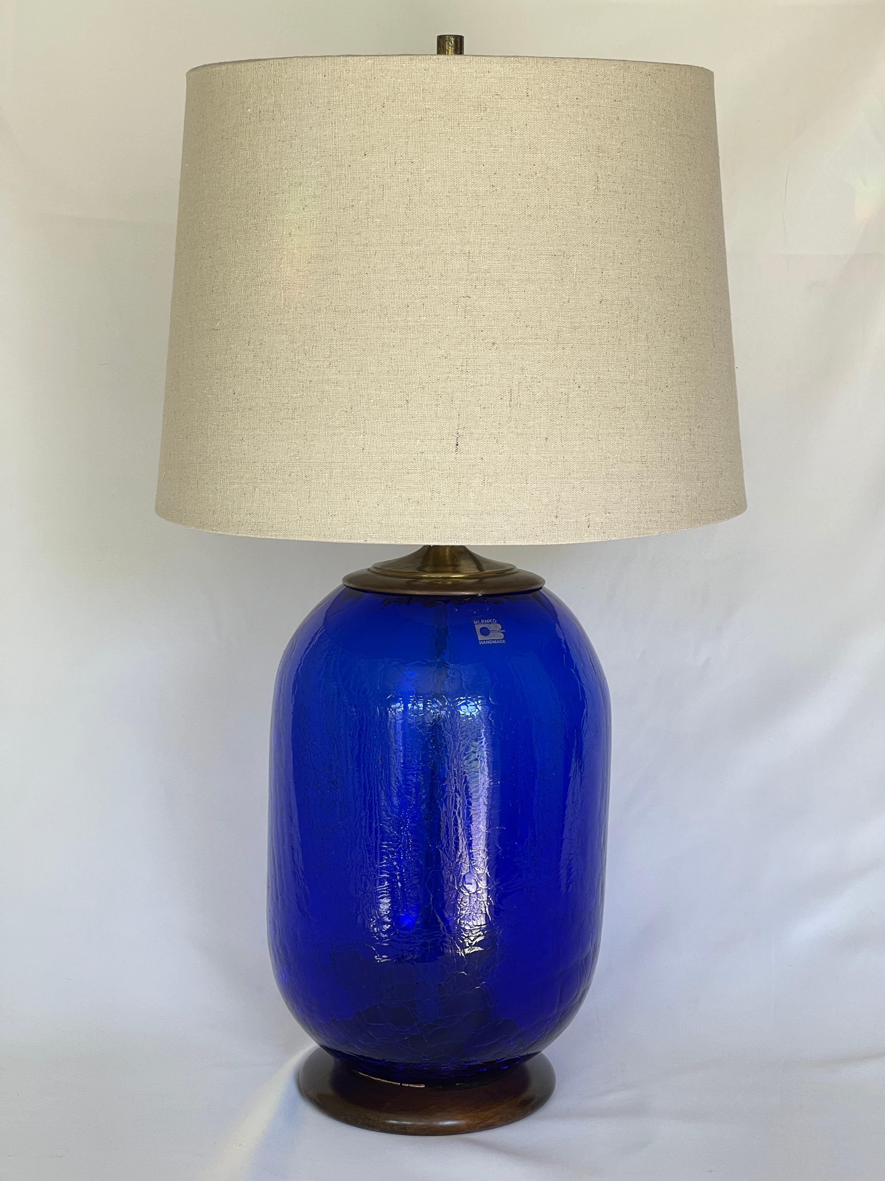 Blenko 1980's craqueliertes blaues Glas Fass Form Lampe mit runden Nussbaum Basis.
Die Originalbeschläge sind mit einer Messingkappe und einer verstellbaren Harfe versehen, die sich an verschiedene Höhen und Lampenschirmgrößen anpassen lässt. Schirm
