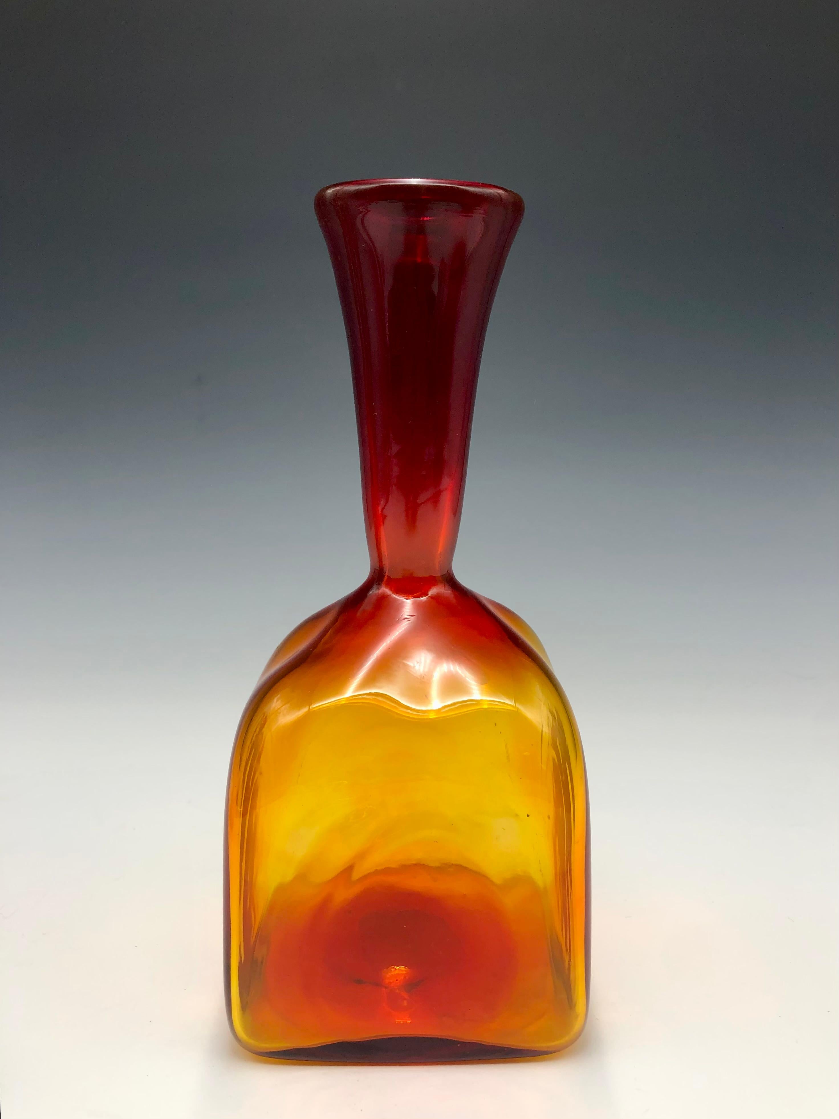Vibrante jarrón cuadrado estriado de vidrio soplado a mano, de color rojo y naranja, estilo Blenko Amberina. Color naranja intenso con sutiles arcos visibles en el cuerpo del jarrón, que se difuminan en rojo hacia el cuello. 

Una llamativa pieza