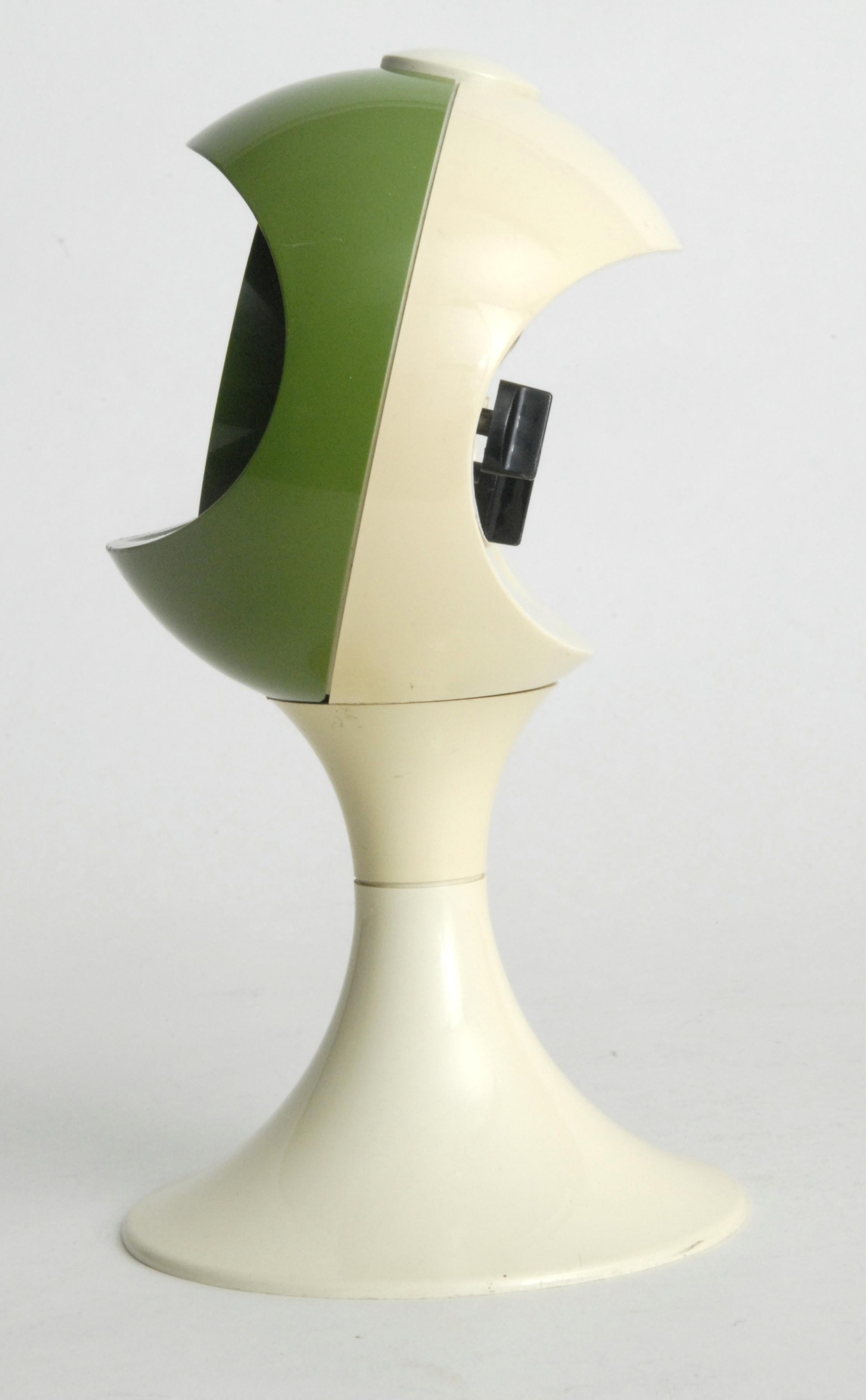 A space race influenced clock design in the form of a helmet in olive green and white. An alarm clock with separate spring mechanisms for the time and alarm winding.