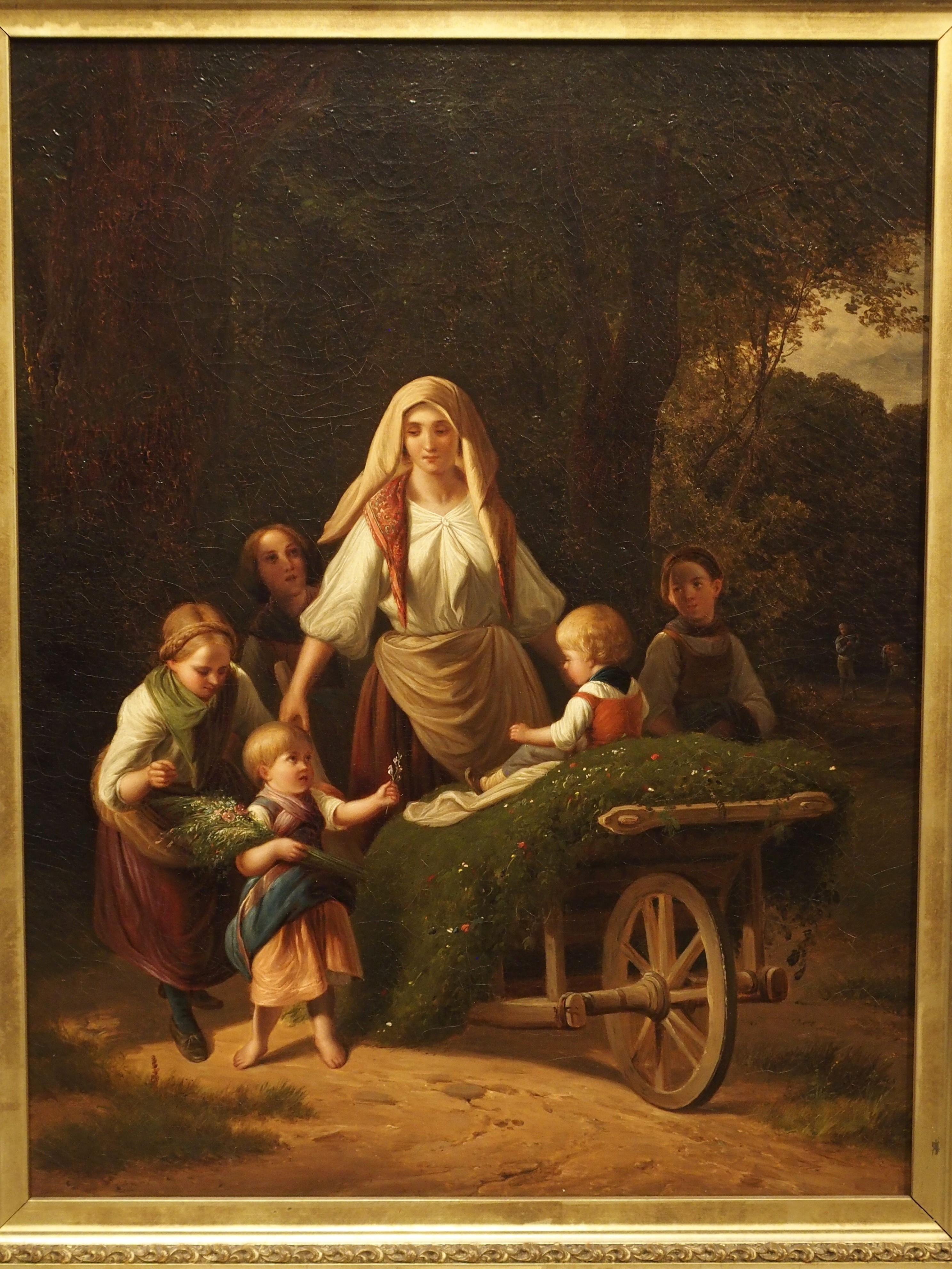 This antique oil painting depicts a warm country scene of a young mother transporting her child in a bed of grasses and flowers, in a wooden wheelbarrow. The artist has perfectly painted the faces of the little girls surrounding the woman, and each