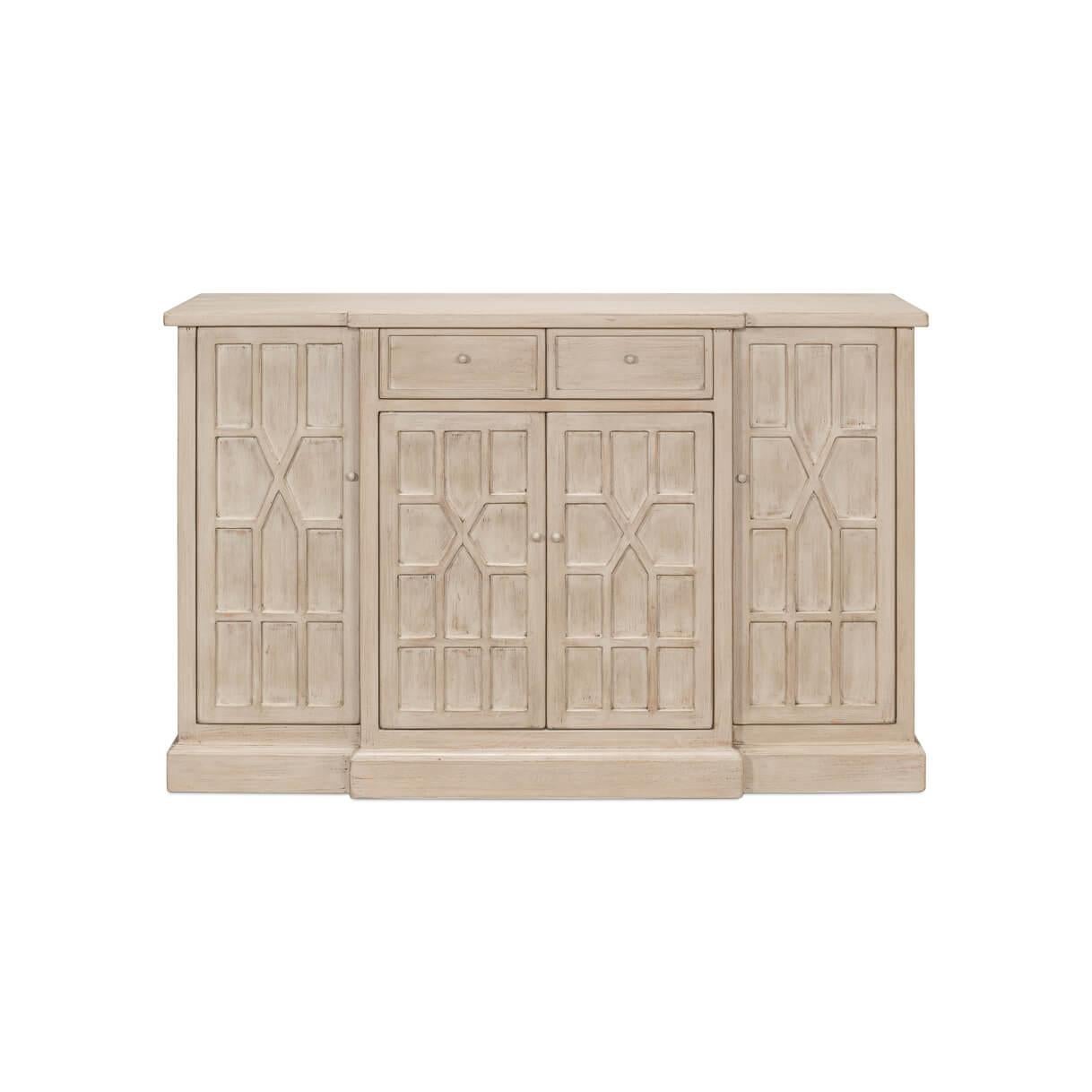 This exquisite piece, with its classic breakfront form is crafted from pine and finished in a lightly distressed Stone gray finish. The intricate geometric Tudor-inspired pattern on the doors draws the eye, adding a dash of architectural finesse to