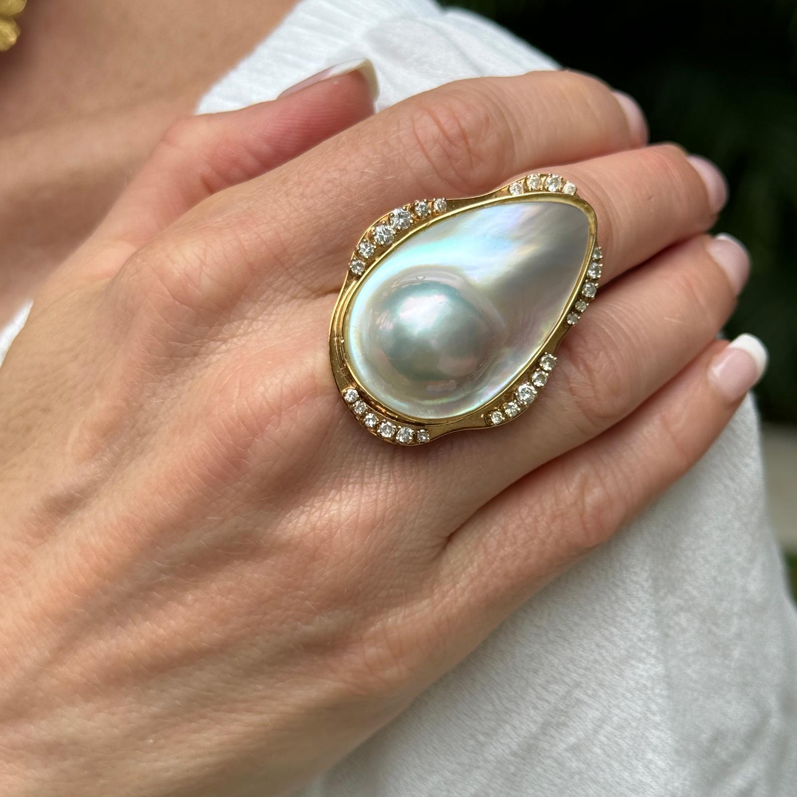 This blister pearl diamond vintage cocktail ring is a captivating piece of jewelry that combines the natural allure of a blister pearl with the brilliance of diamonds, all set in warm 14 karat yellow gold. At the center of the ring sits a blister