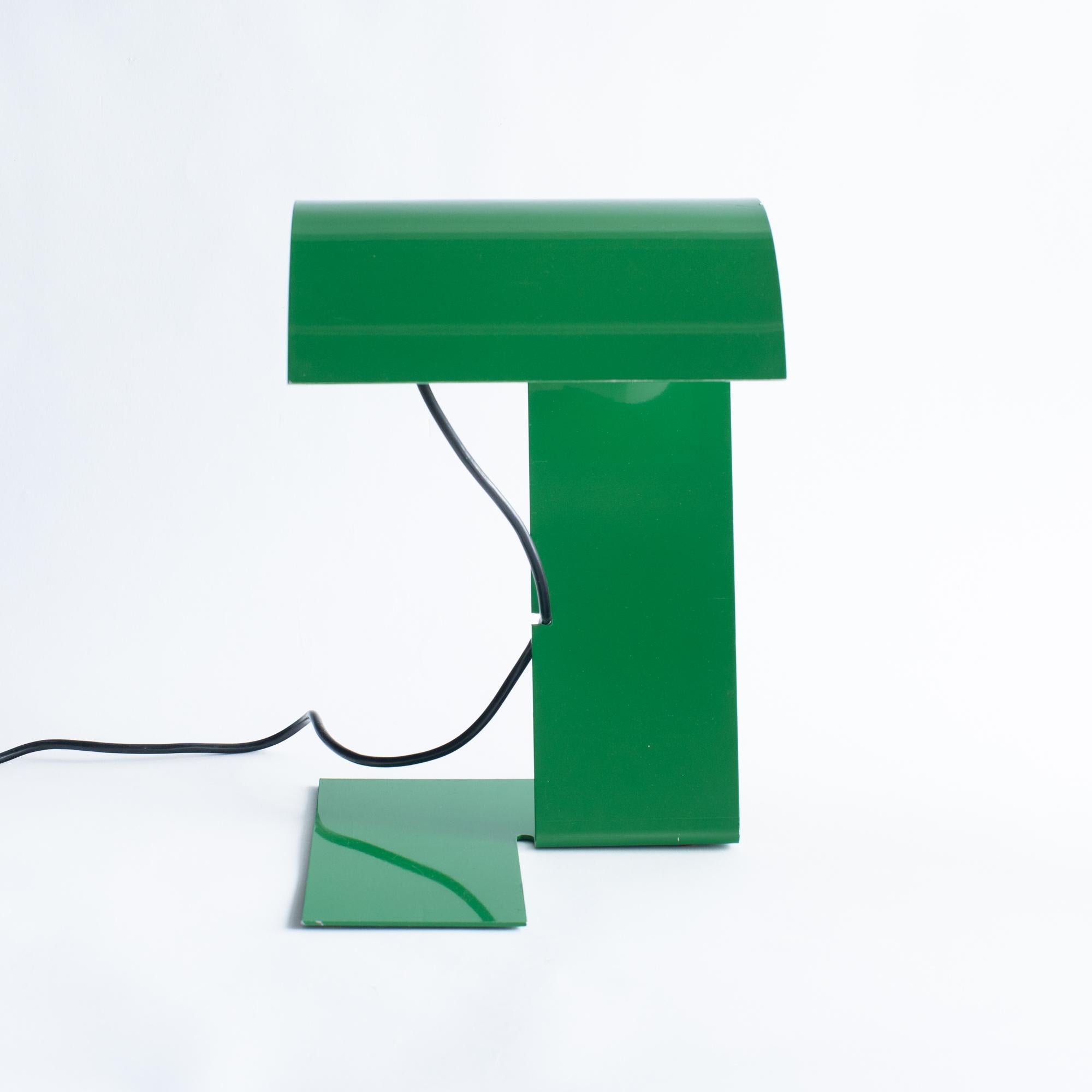 Lámpara de mesa o escritorio de acero diseñada por Trabucco, Vecchi, Volpi para Stilnovo. Se diseñó en los años 70. El color es verde y el cable negro. 
Forma escultórica realizada doblando una plancha de acero. 

Probablemente pieza de producción
