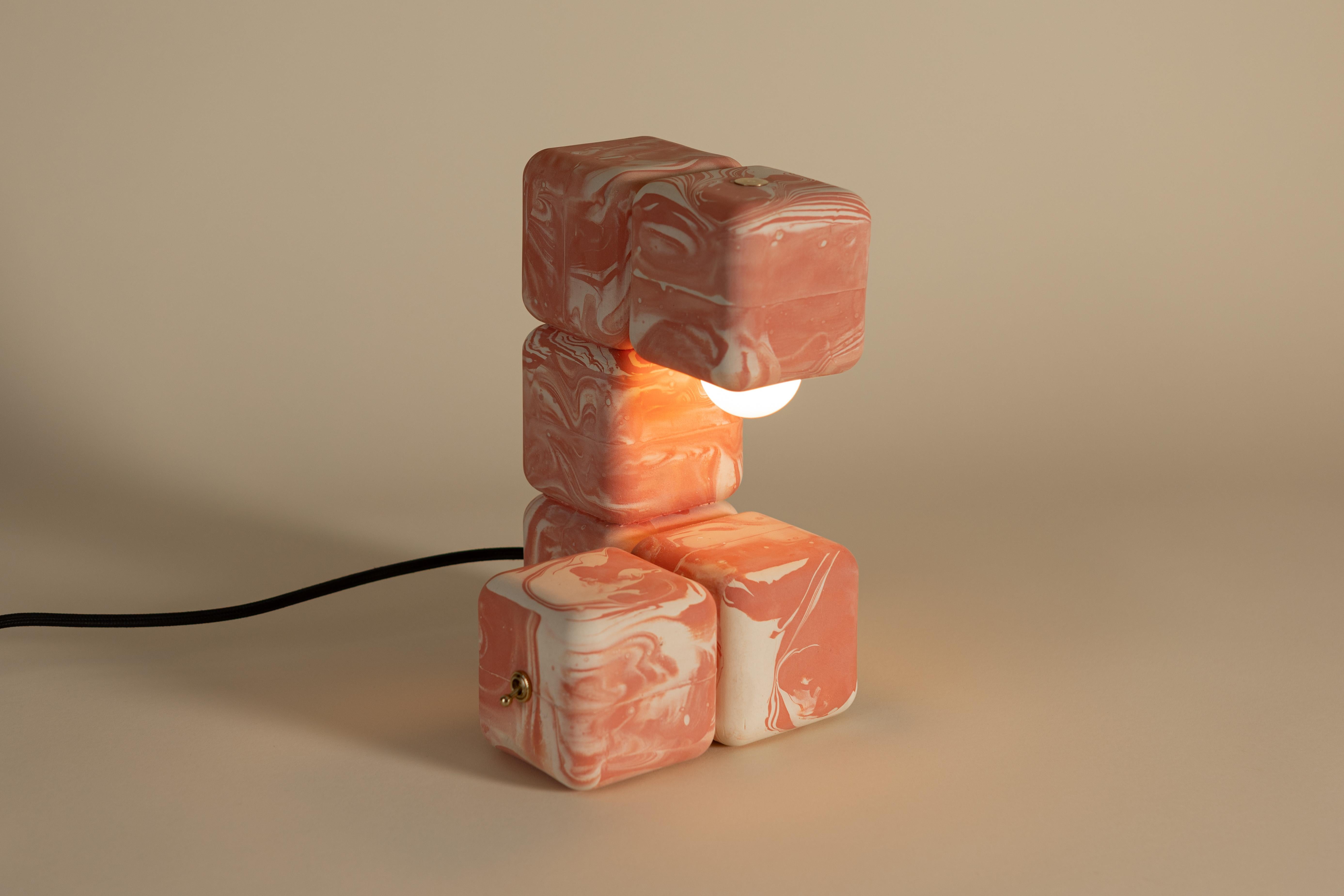 La Lámpara de Mesa Blocky aporta una energía lúdica a la mesa, a la vez que destila estructura en formas mínimas: cubos apilados con bordes suavizados, dispuestos rítmicamente. Asomando por el cubo final, la bombilla proyecta una cálida cascada de