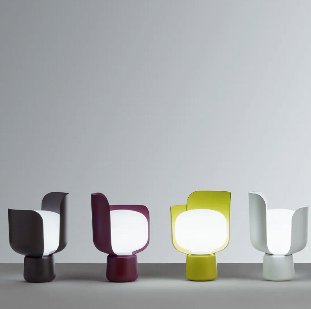 Table lamp with diffused light adjustable by moving the petals. Frame made of painted aluminium with polycarbonate petals. Diffuser made of milk-white and opaline polyethylene. Transparent power cable, plug and switch. European two-pole plug. Bulb