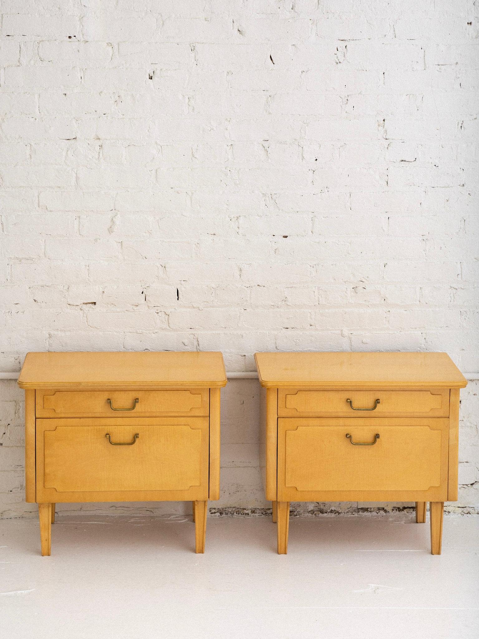 A pair of blonde wood nightstands. One upper drawer and lower drop front cupboard. Brass hardware. Lacquered blonde finish. Unmarked.